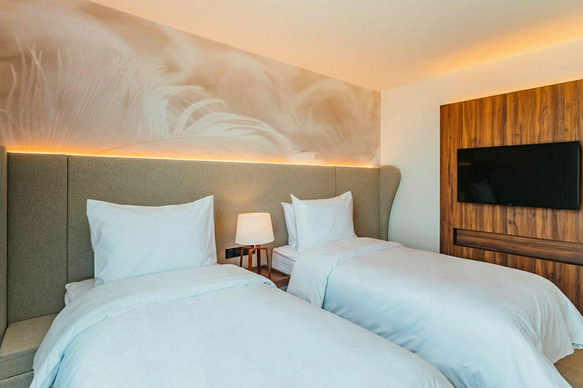 Bild av ett hotellrum med två separata sängar, en lampa och en TV på väggen. (AI-genererad text)