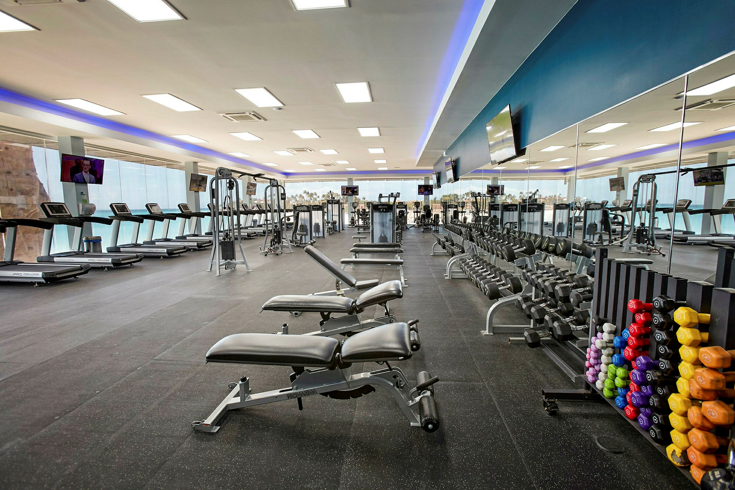 Ett gym med träningsutrustning såsom löpband, hantlar och träningsmaskiner. På ena sidan syns en spegelvägg. (AI-genererad text)