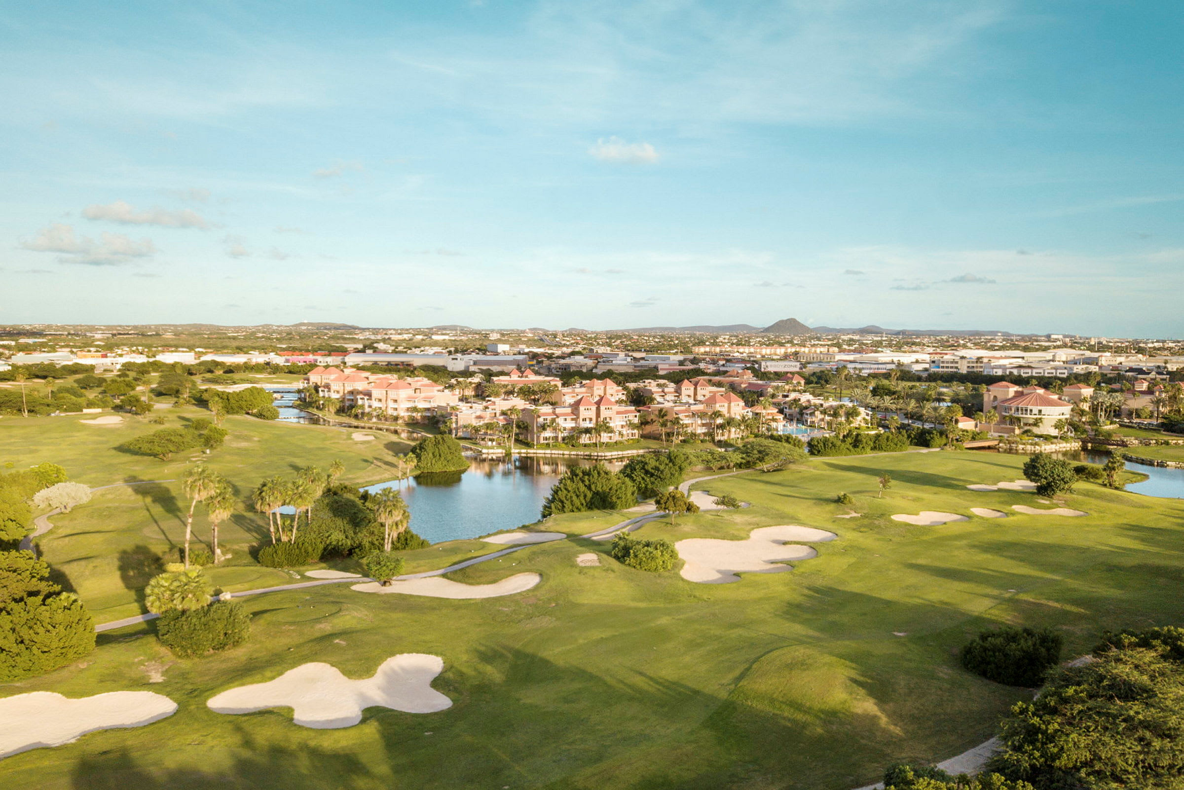 En golfbana med sandbunkrar och grönska, intill ett bostadsområde nära vatten. (AI-genererad text)