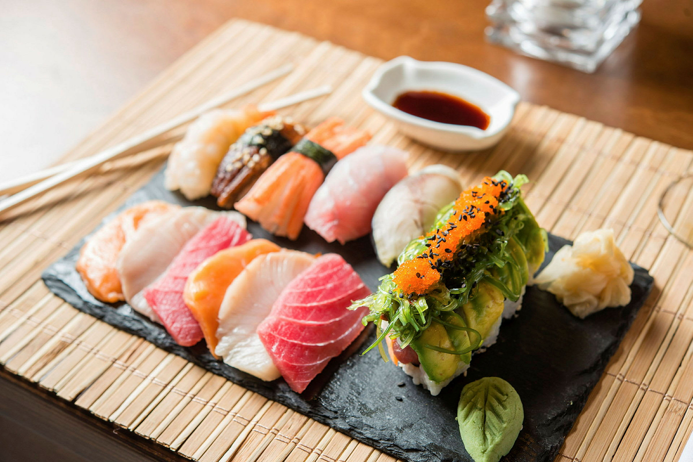 En skifferbricka med olika sorters sushi, wasabi och inlagd ingefära, samt sojasås i en skål. (AI-genererad text)