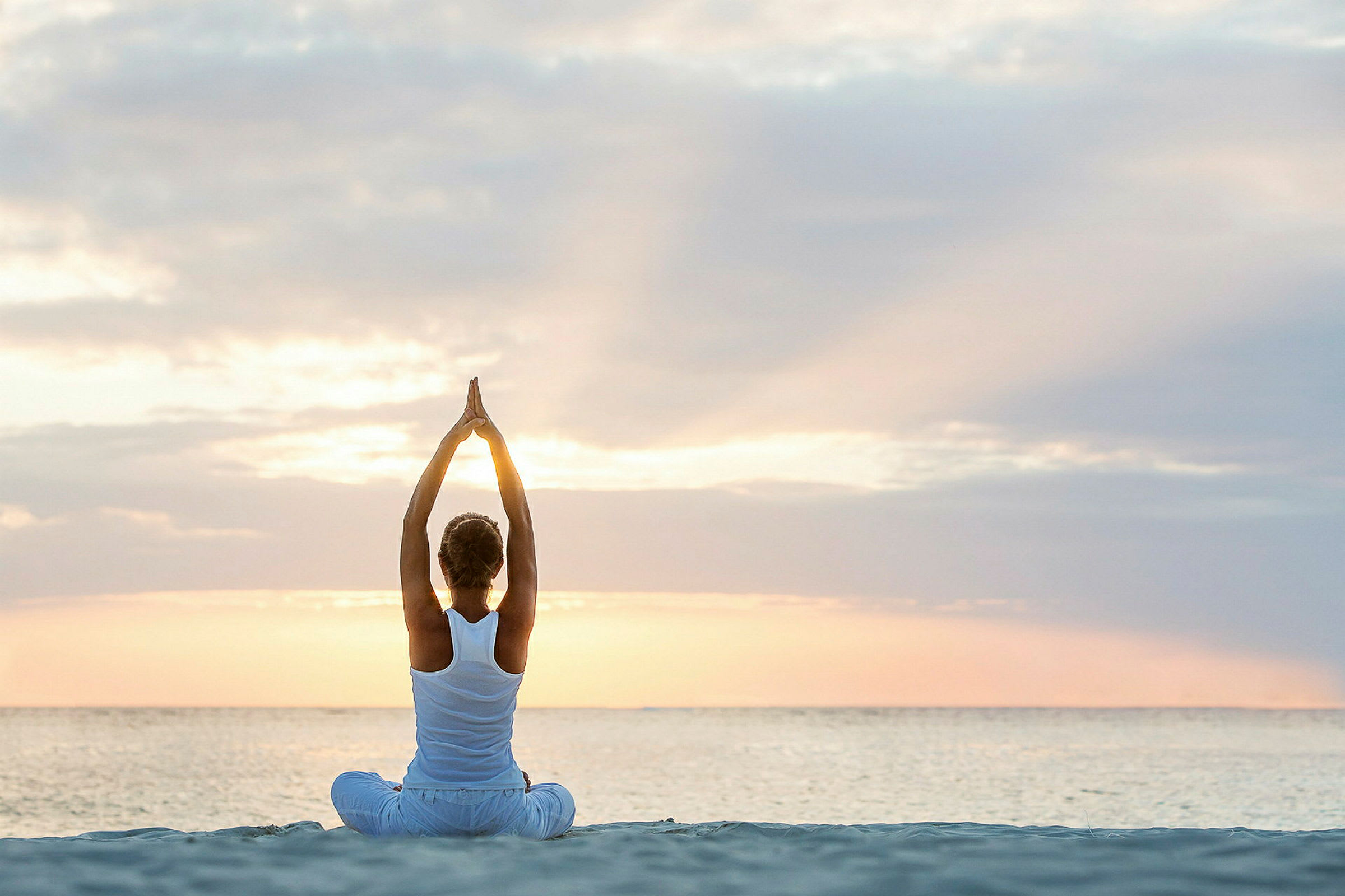 En person som sitter på stranden i soluppgången och gör yoga med armarna uppsträckta. (AI-genererad text)