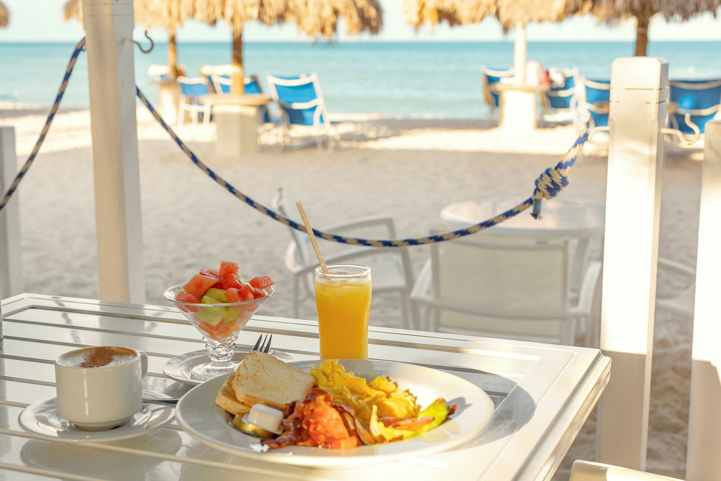 Frukost på ett bord med utsikt över havet och strandstolar. (AI-genererad text)