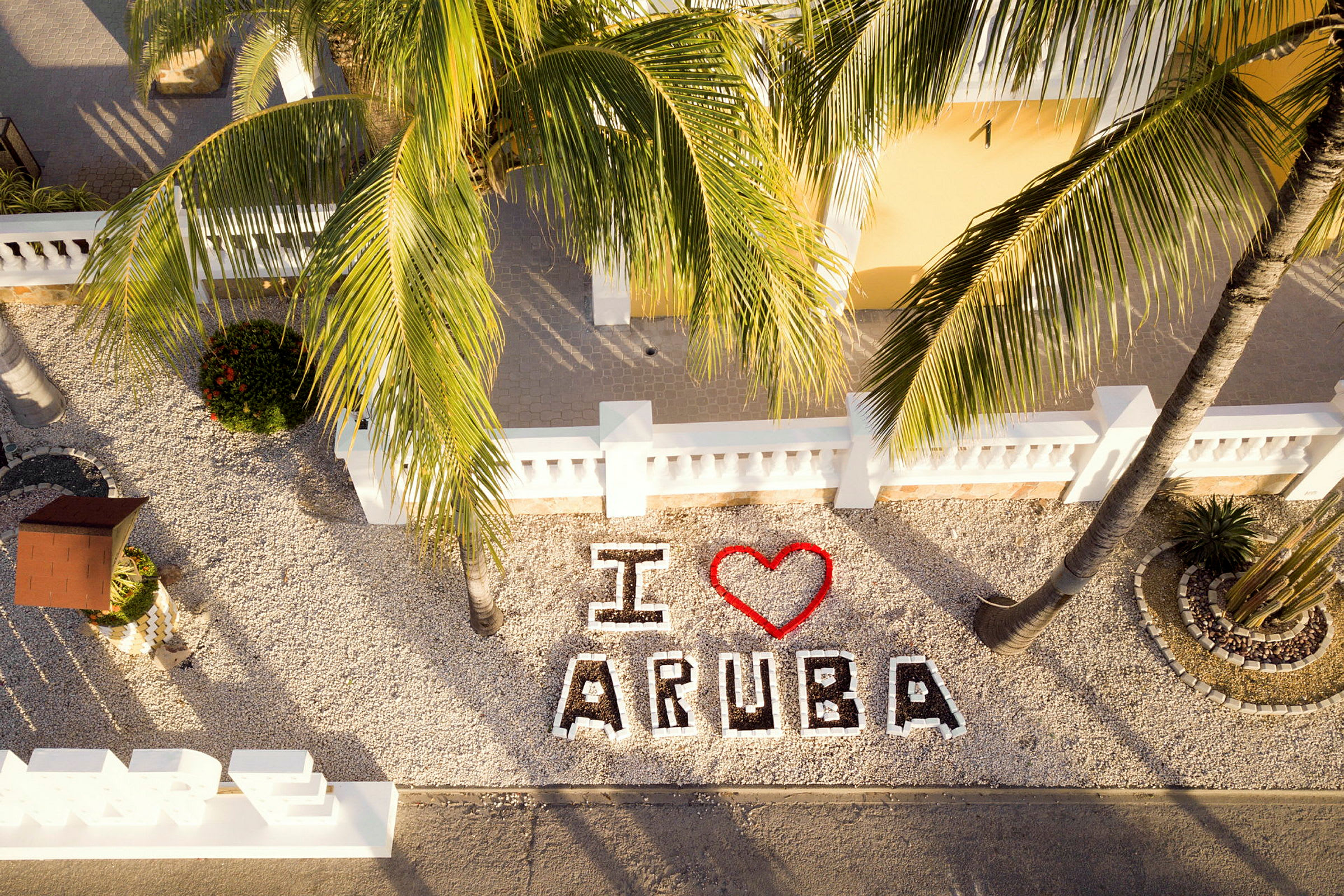 Texten "I ❤️ Aruba" är synlig bland dekorativa stenläggningar och palmer. (AI-genererad text)