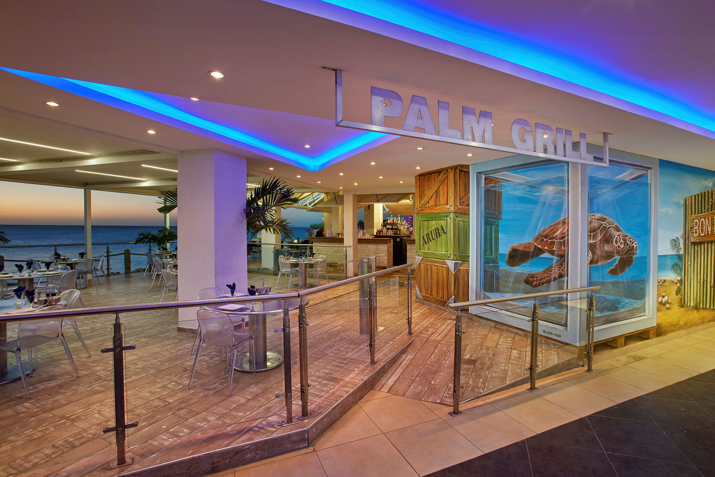 Interiör av en restaurang med havsutsikt, uteservering och en skylt med texten "Palm Grill". Väggarna är dekorerade med målningar, bland annat en sköldpadda. (AI-genererad text)