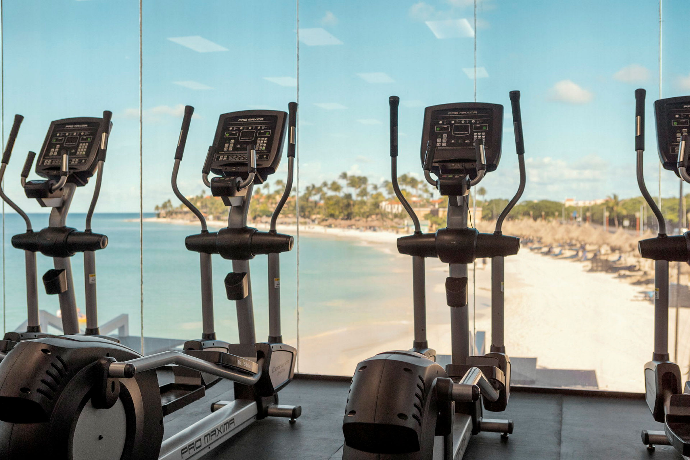 Träningscyklar i ett gym med utsikt över en sandstrand och havet. (AI-genererad text)