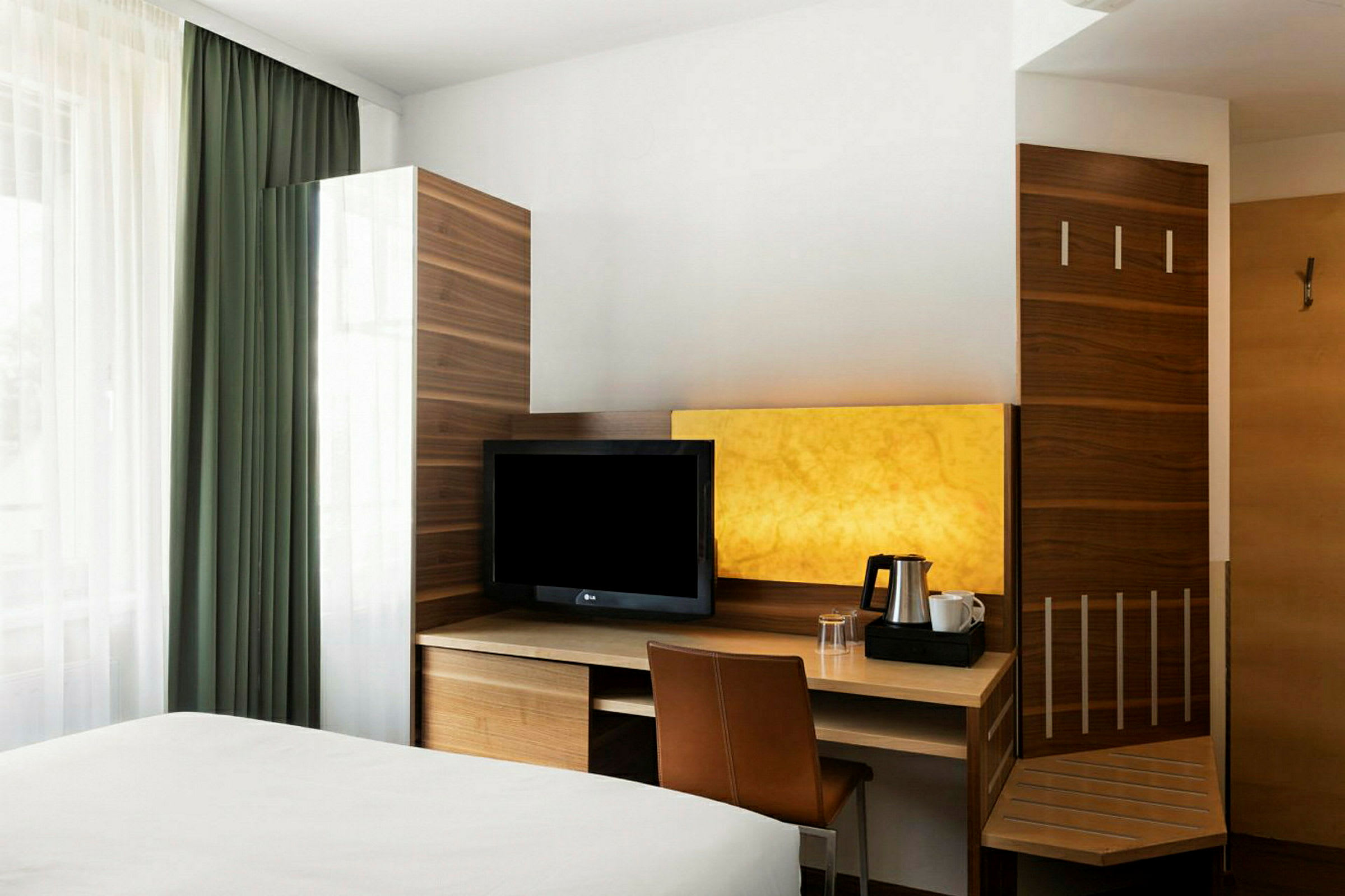 Ett hotellrum med en säng i förgrunden, ett skrivbord med en TV och en tillhörande stol, samt en vägg i trä och en lysande gul nyans. (AI-genererad text)