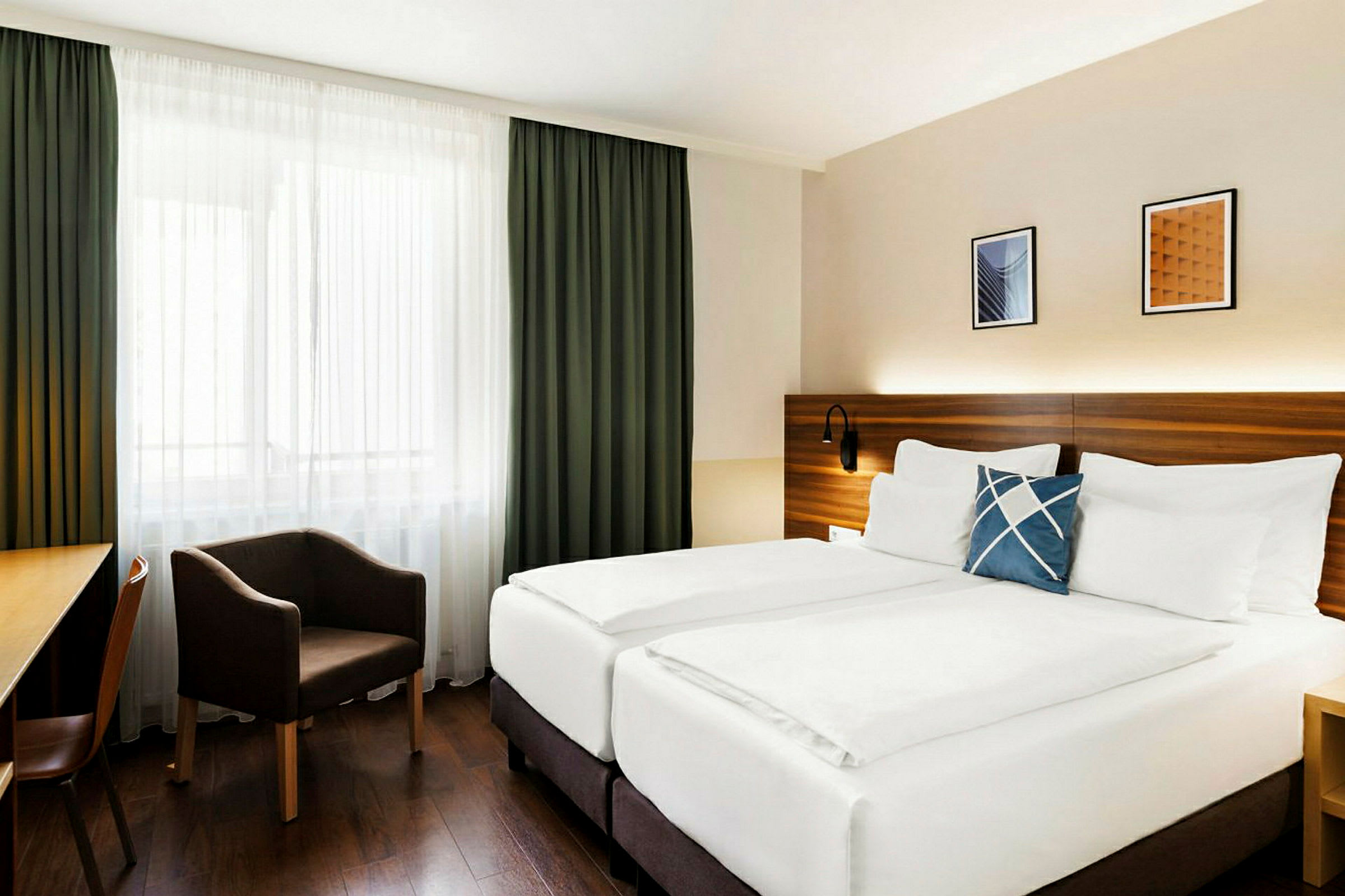 Ett hotellrum med en dubbelsäng, en fåtölj och ett skrivbord. Fönstret är dekorerat med gardiner. (AI-genererad text)