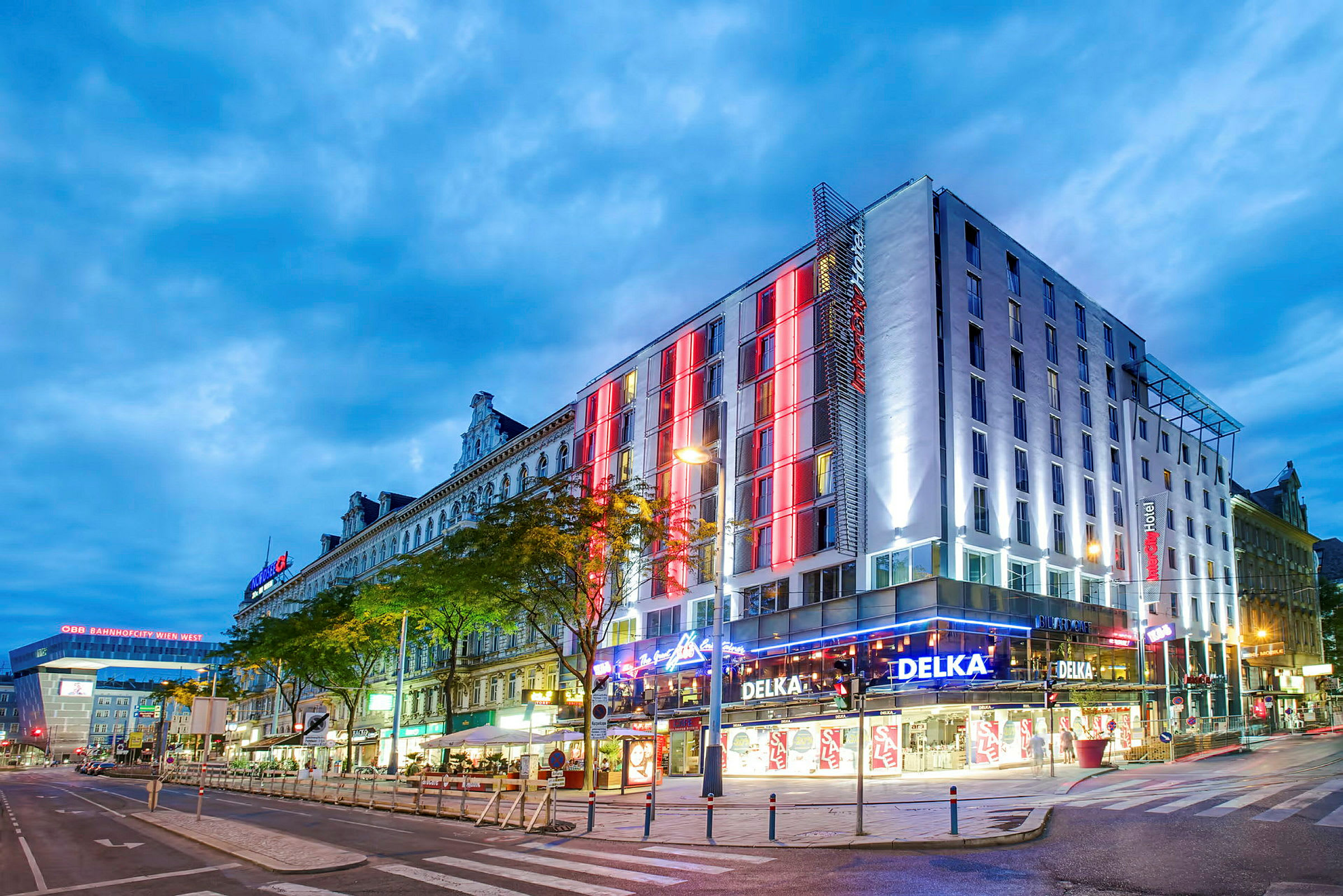 En stadsmiljö med en modern byggnad, belyst med färgade ljus och omgiven av gator. (AI-genererad text)