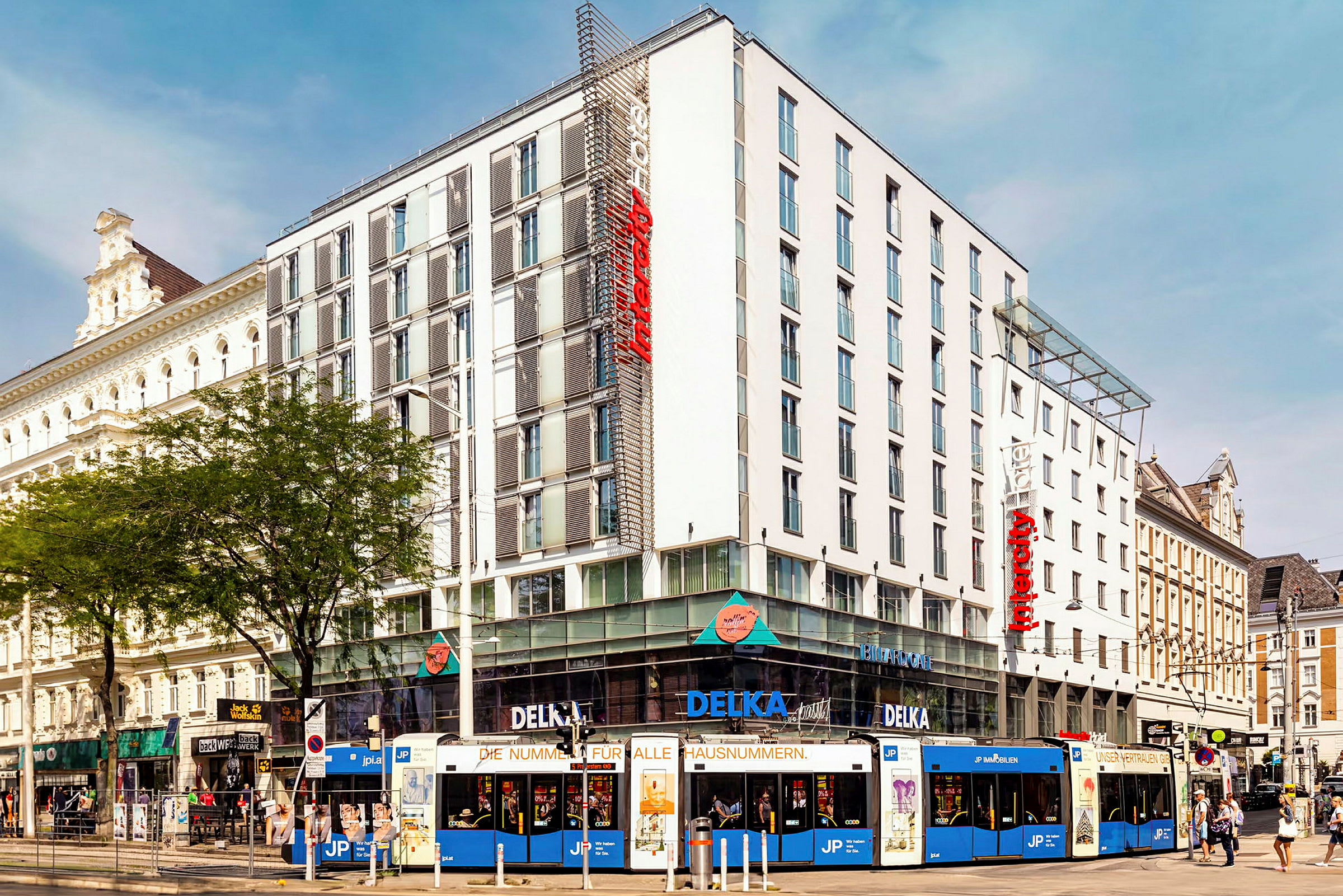 En flerfärgad spårvagn framför ett modernt hotell i stadslandskap. (AI-genererad text)