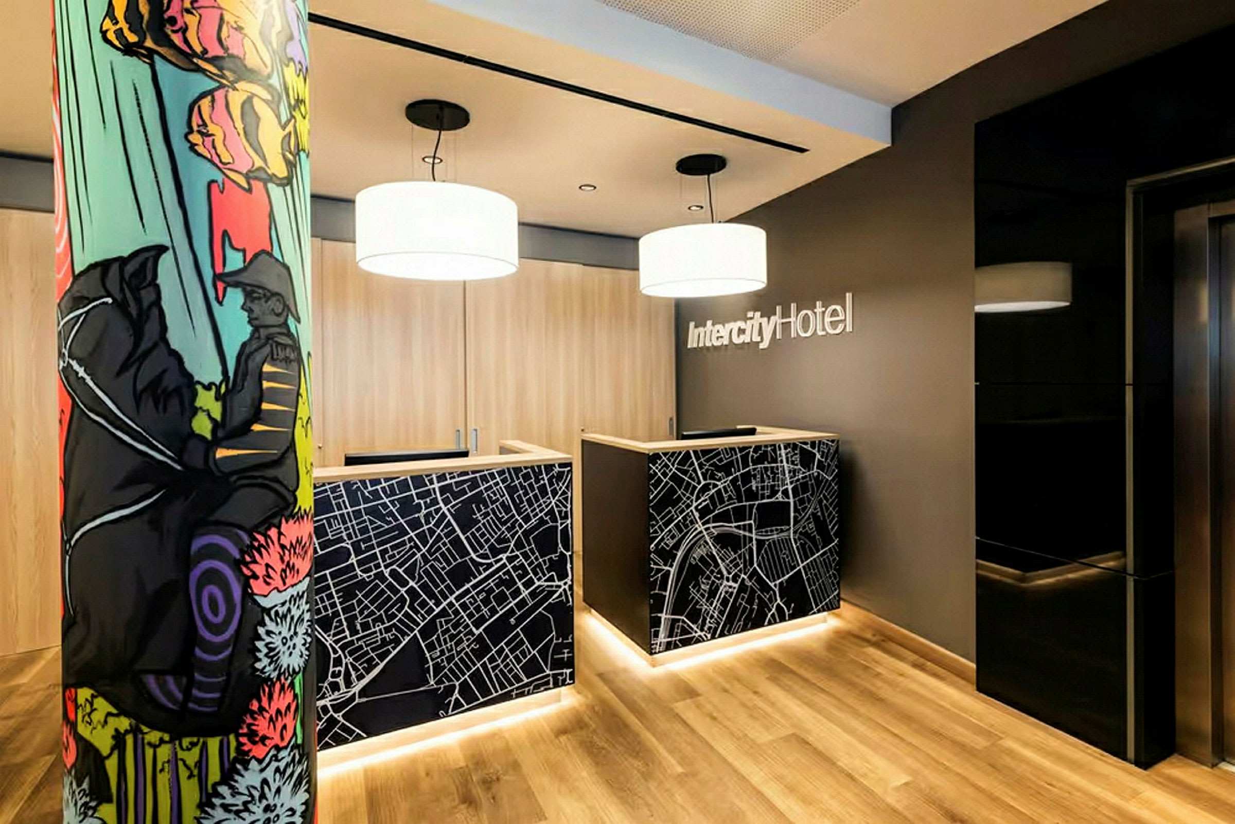 Receptionen med två receptionsdiskar dekorerade med kartmotiv i en lobby på IntercityHotel. En färgglad pelare syns till vänster. (AI-genererad text)