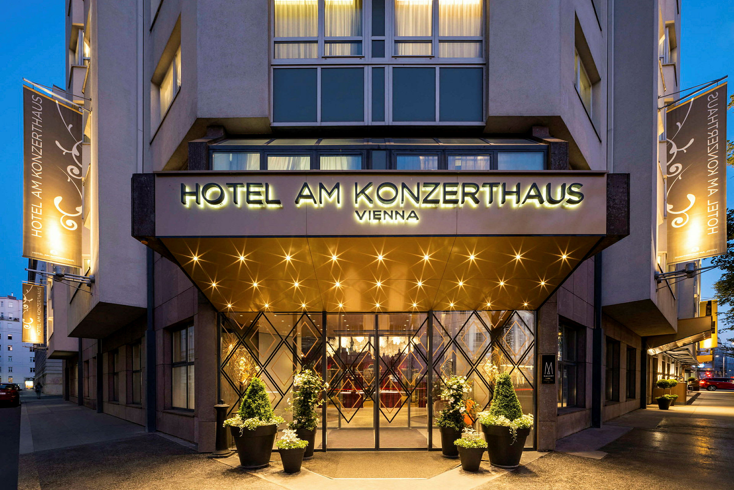 Entrén till ett hotell med en skylt som lyder "Hotel am Konzerthaus Vienna". Belysning och dekorationer syns runt ingången och på fasaden. (AI-genererad text)