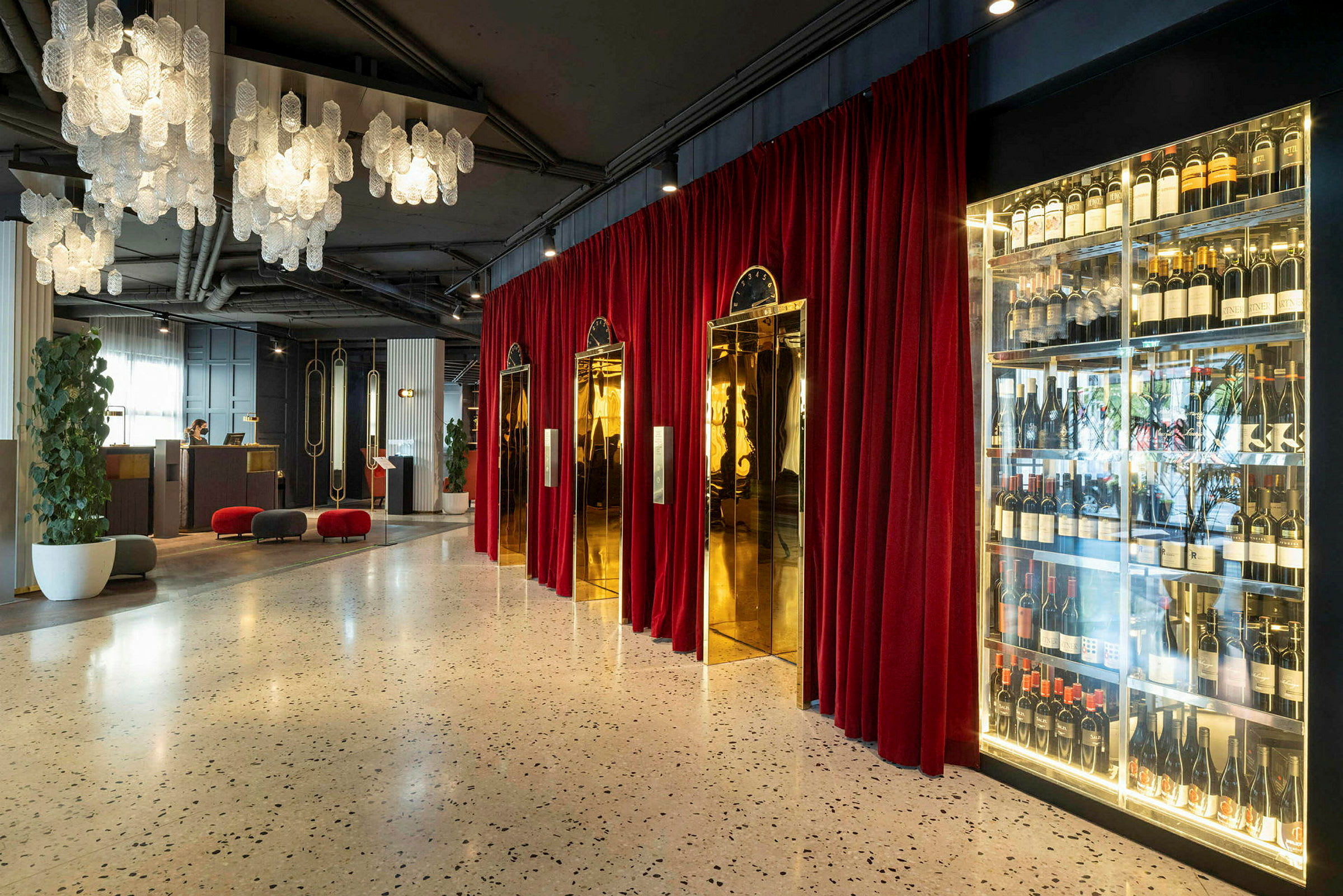 Hotellobby med hängande ljuskronor, röda gardiner, gyllene hissdörrar och en vinförvaring. (AI-genererad text)