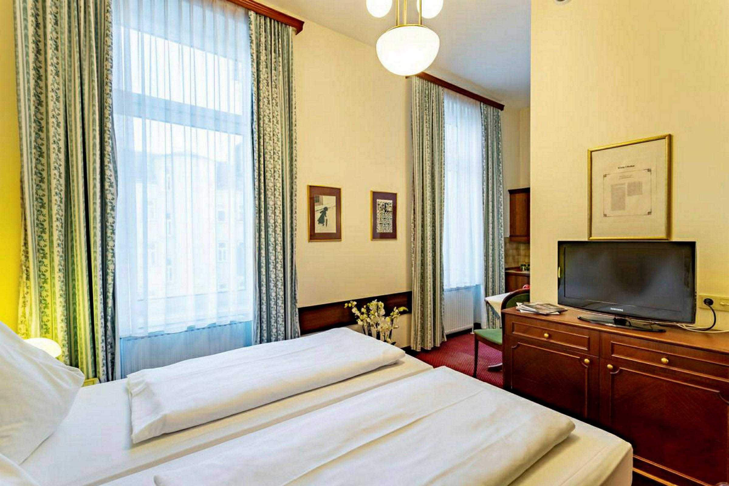 Interiör av ett hotellrum med en dubbelsäng, en TV på en träbyrå och två stora fönster med gardiner. (AI-genererad text)