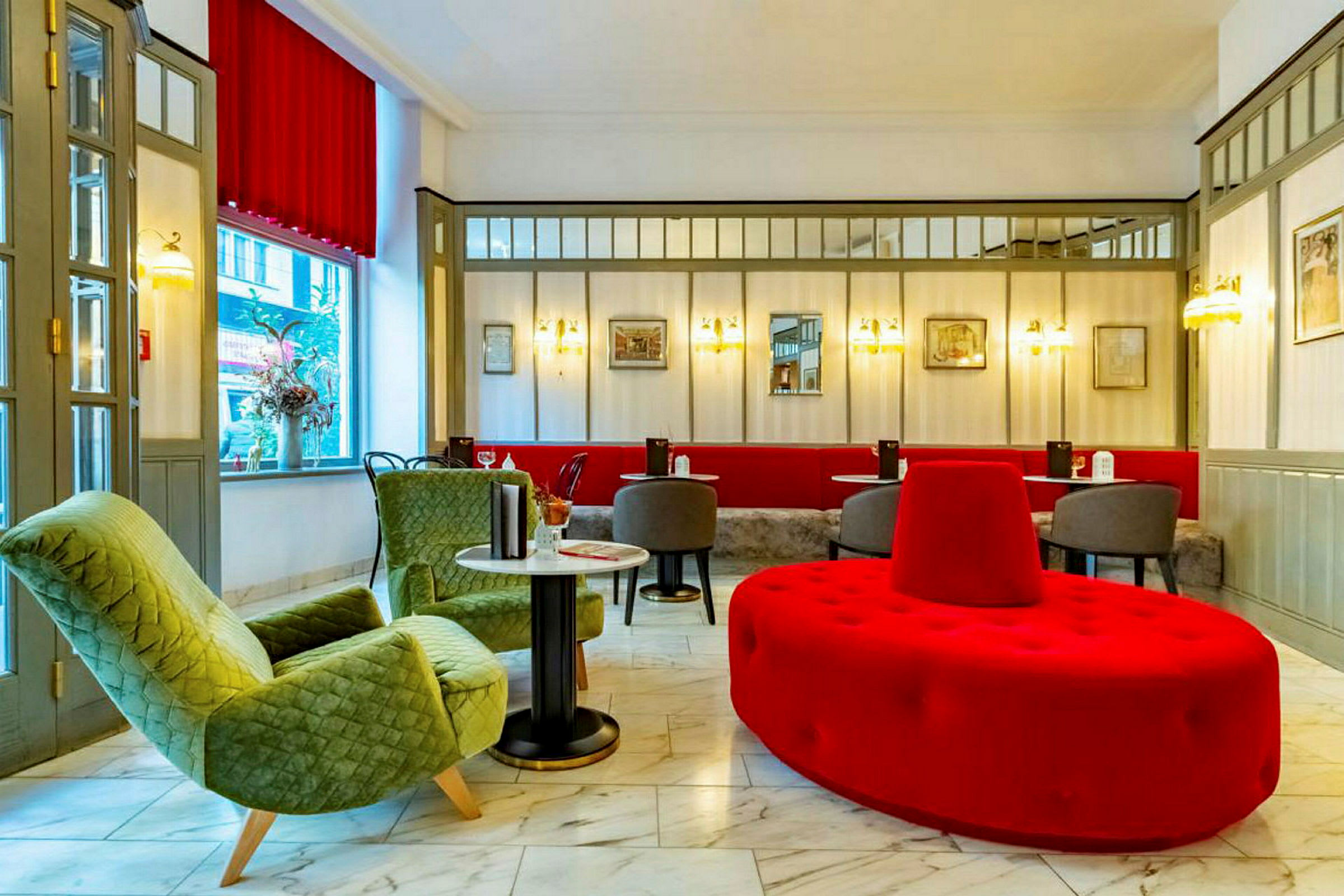 En hotellobby med sittgrupp inkluderande gröna fåtöljer, röda och gråa sittmöbler och marmorgolv. (AI-genererad text)
