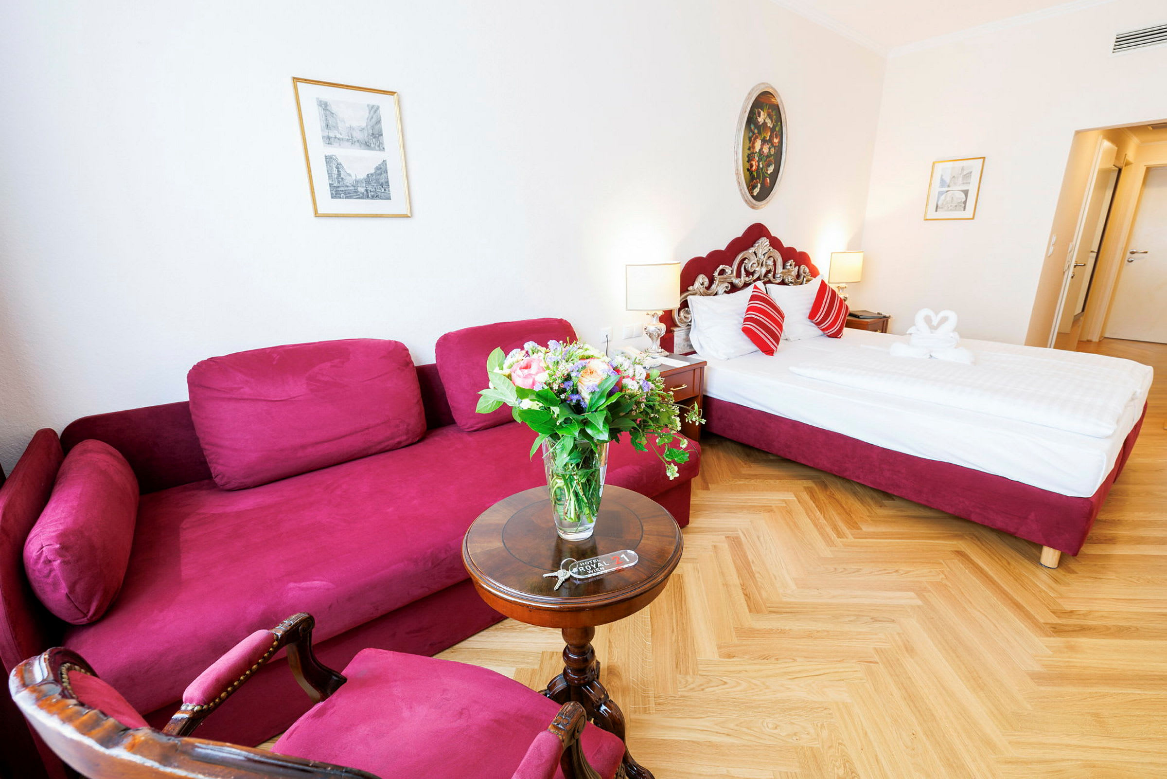 Ett hotellrum med en röd soffa, ett runt bord med en blomsterbukett och en säng med röda detaljer. (AI-genererad text)