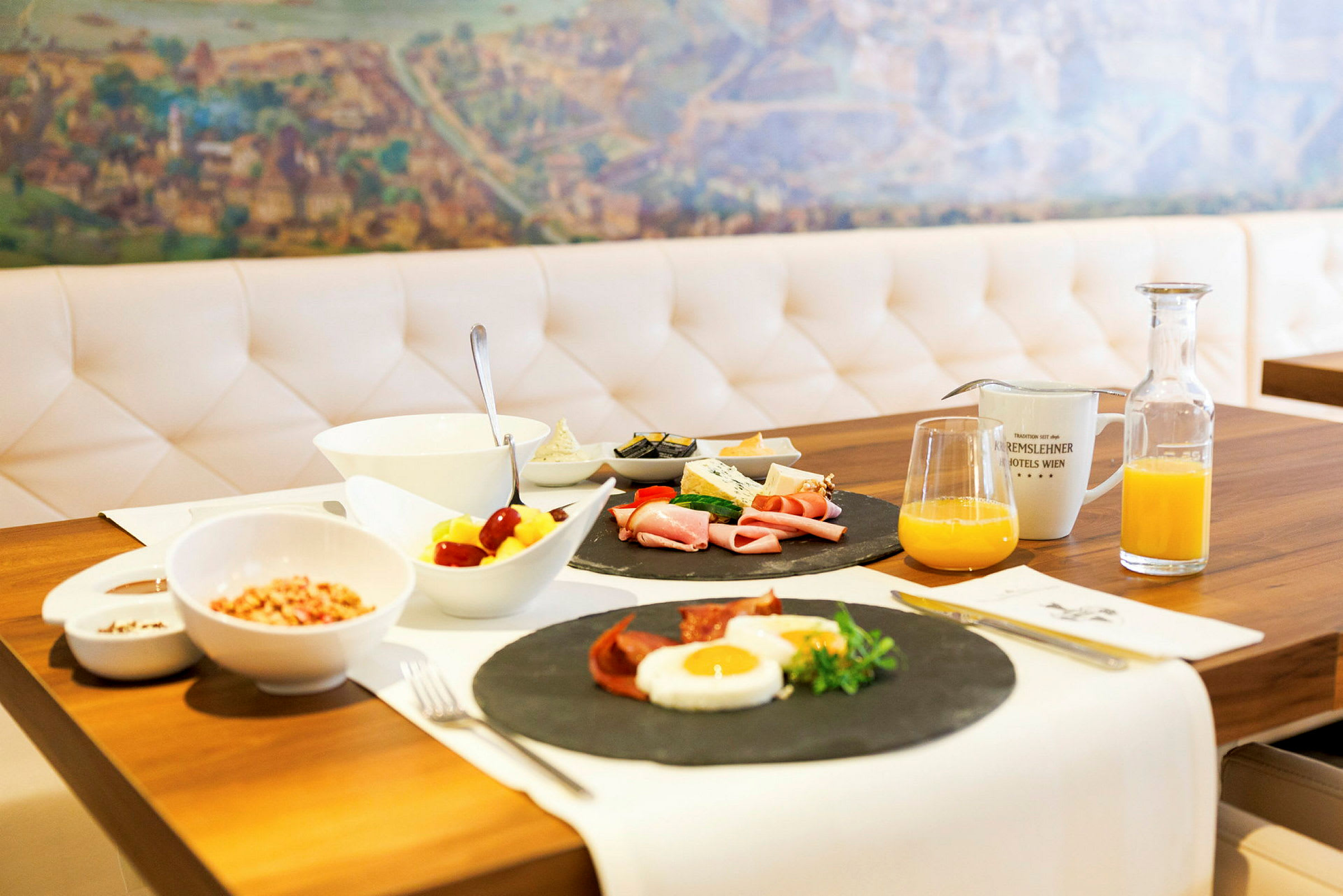 En frukost dukad på ett bord med diverse maträtter, hoppande ägg, kallskuret och grönsaker, samt juice och kaffe. (AI-genererad text)