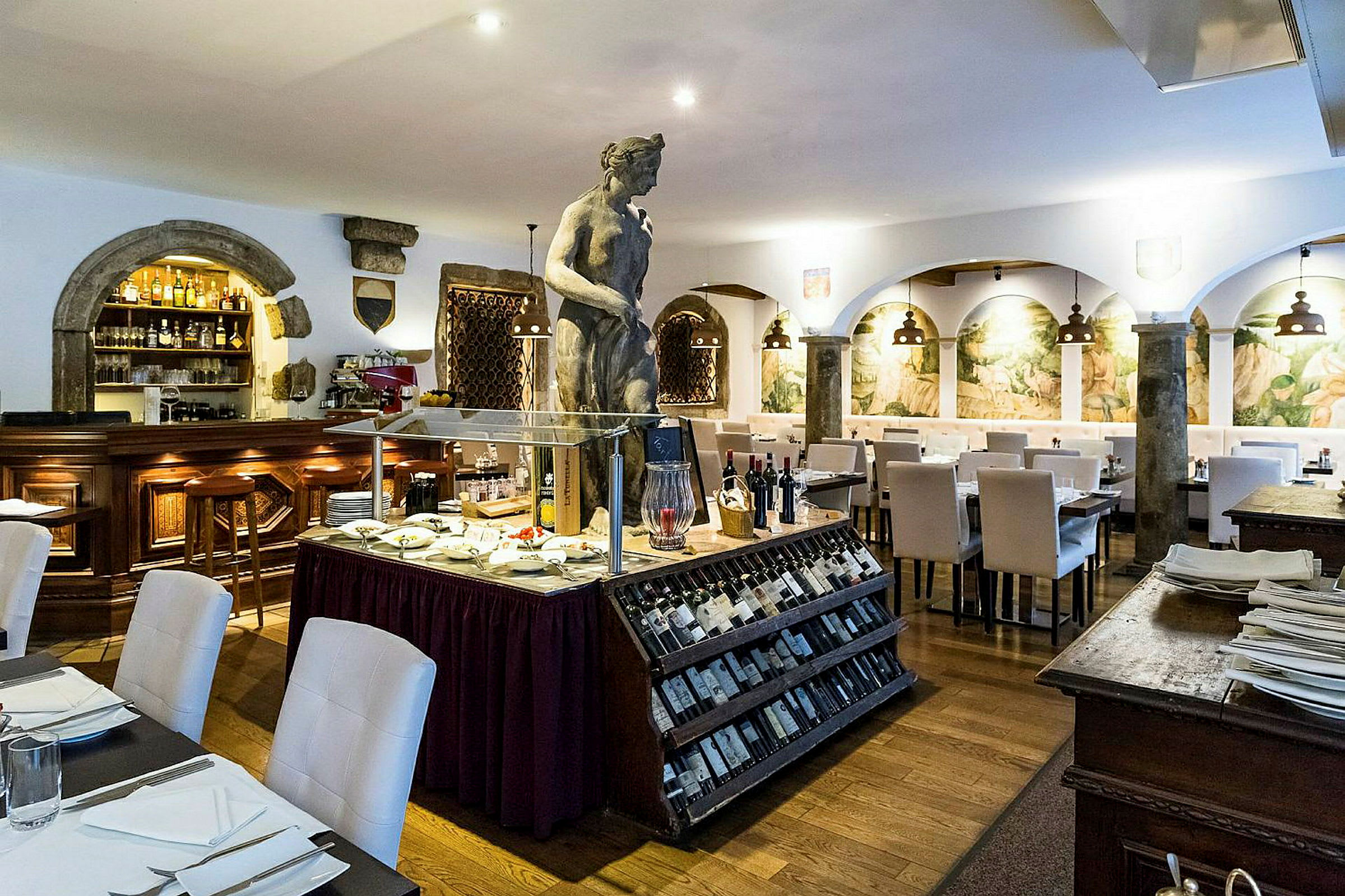 En restaurang med vit inredning, en skulptur i mitten, och en display med viner och delikatesser. (AI-genererad text)