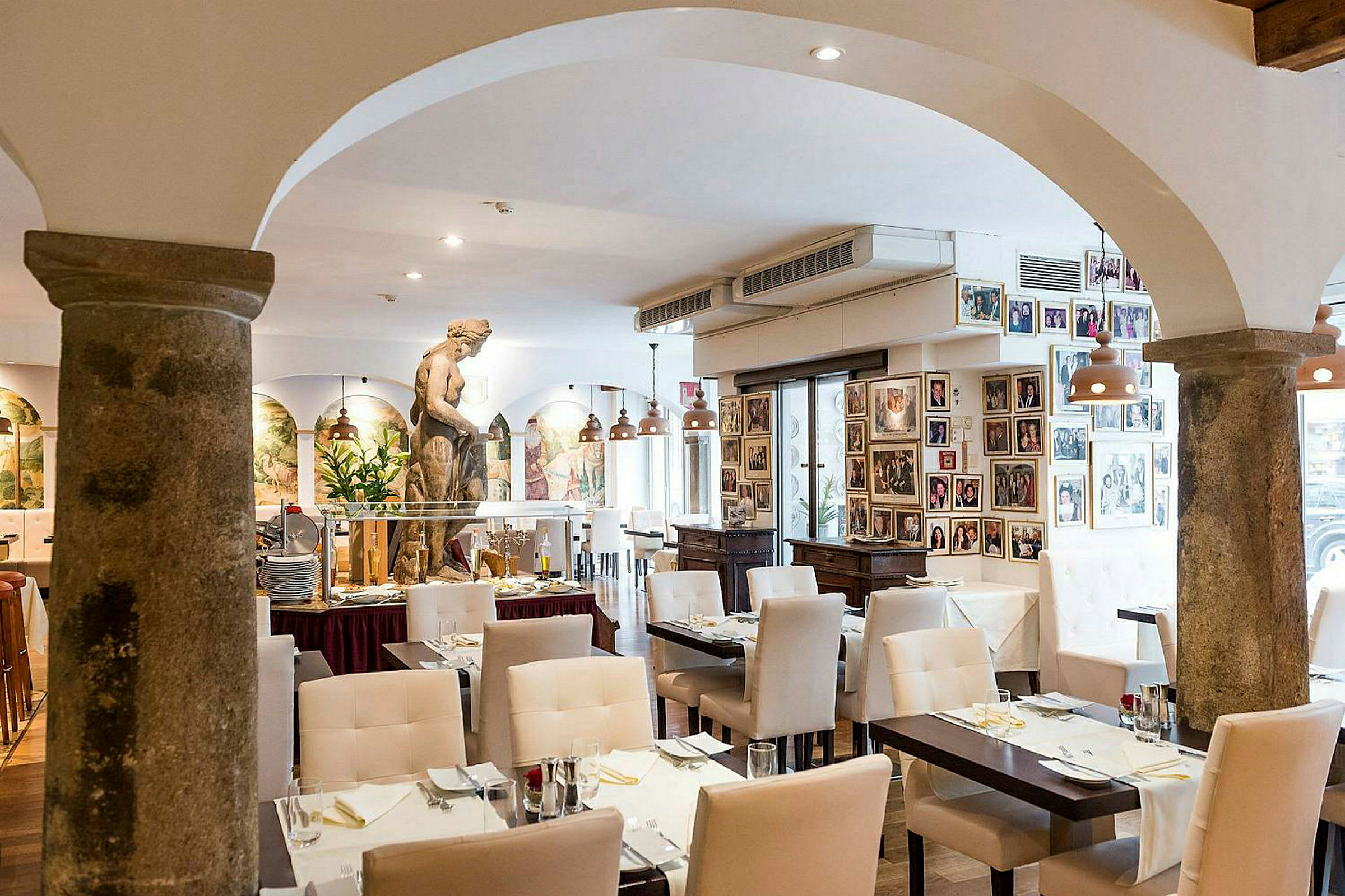 Interiör av en restaurang med vita stolar, dukade bord och en skulptur i mitten av rummet. (AI-genererad text)