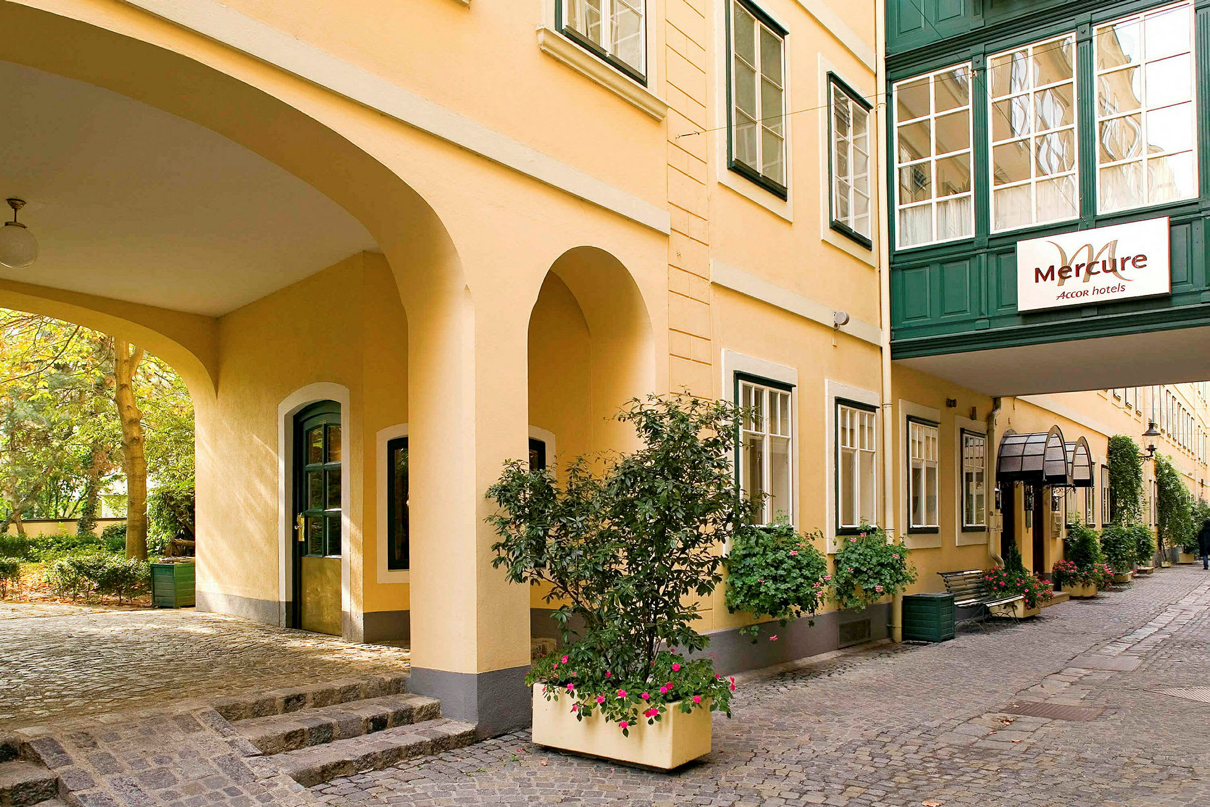En innergård vid hotell Mercure med gula väggar och gröna fönsterkarmar, dekorerad med blommor och grön vegetation. (AI-genererad text)