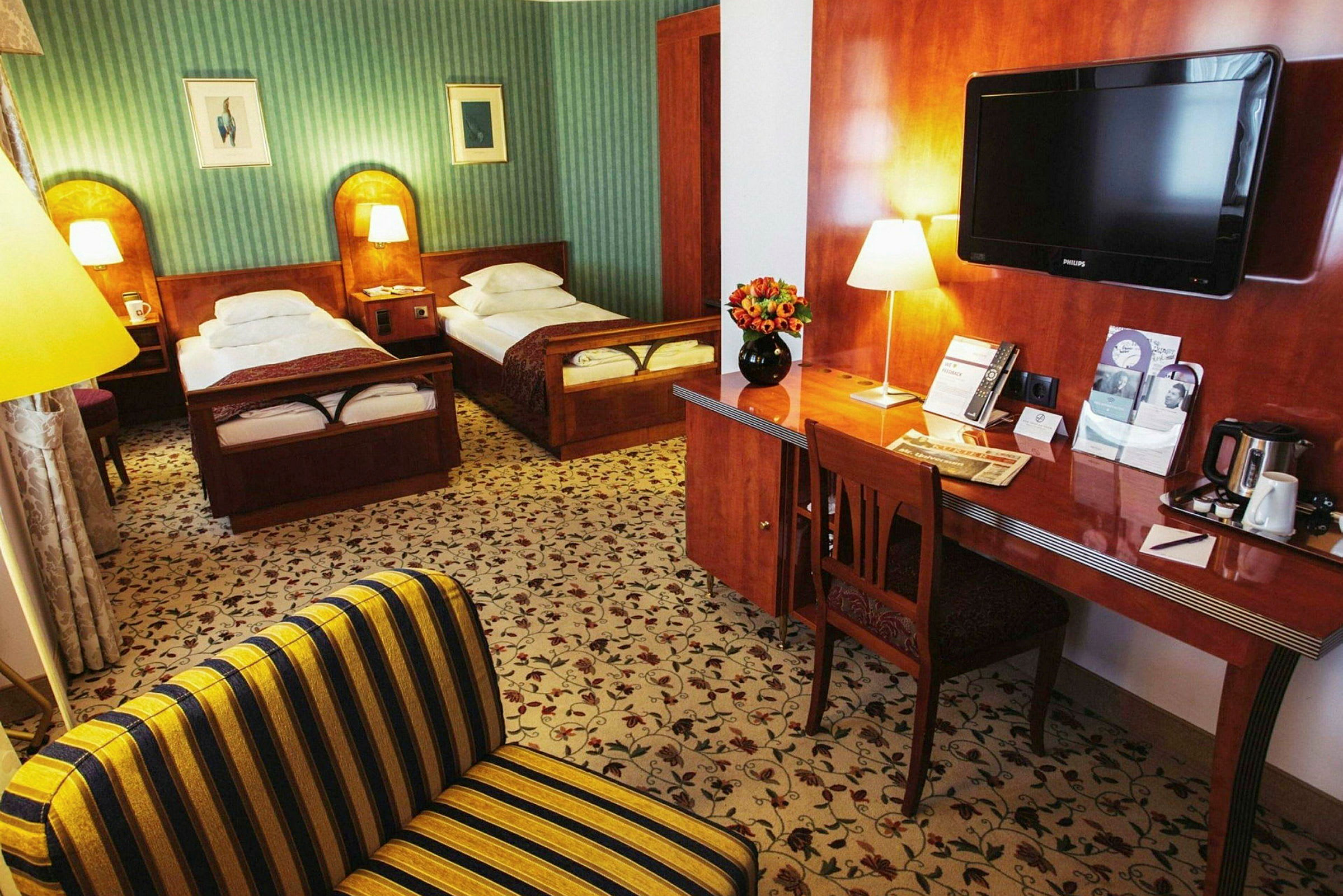 Ett hotellrum med två enkelsängar, en skrivbord med blommor och en TV. (AI-genererad text)