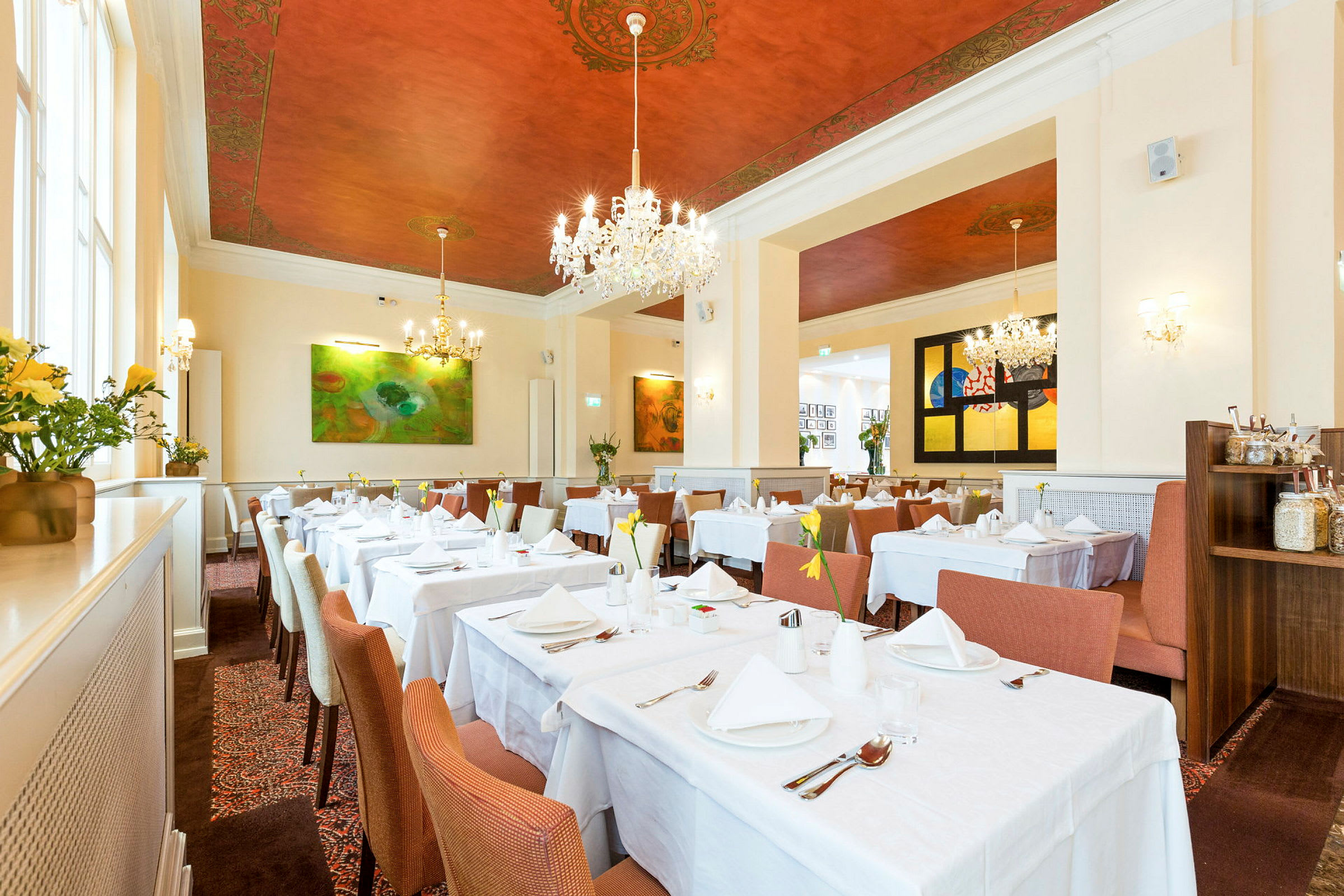 Interiör av en elegant restaurang med vita dukar på borden, stilrena stolar och dekorativt målat tak. (AI-genererad text)