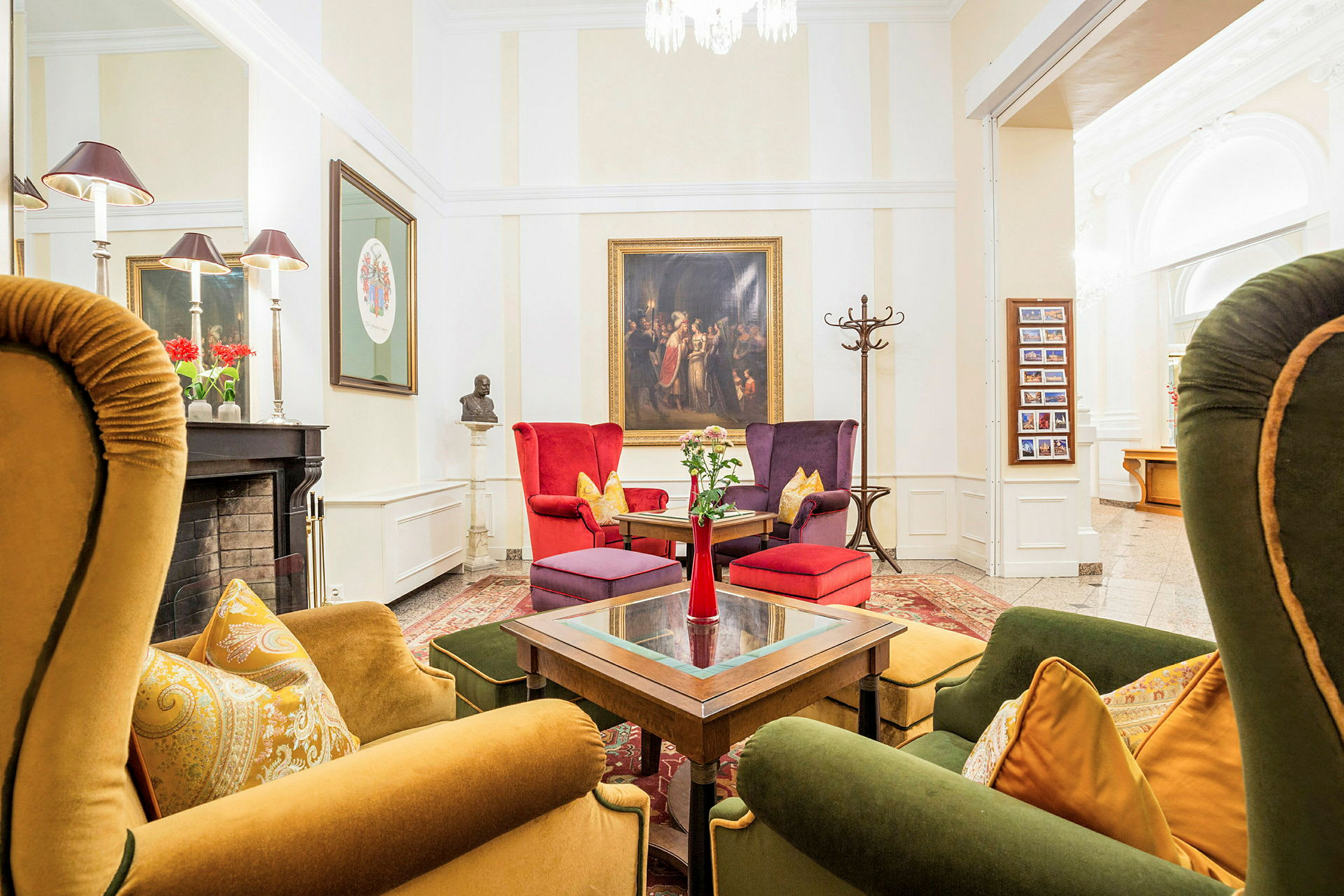 En stilfullt inredd lounge med färgstarka fåtöljer och soffor kring ett bord. Väggarna pryds av konst, och en eldstad med dekorationer syns på sidan. (AI-genererad text)