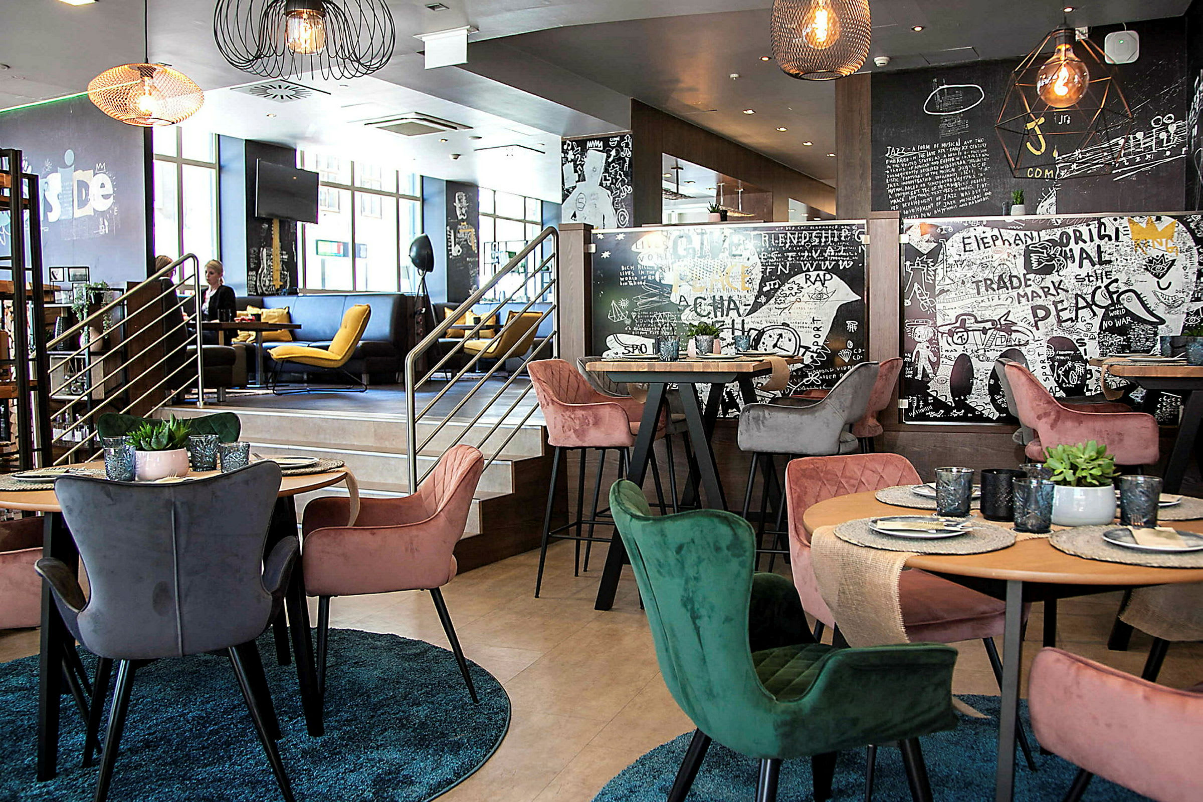 En modern interiör av en restaurang med färgglada stolar runt bord som har dukade tallrikar och glas. Väggarna är dekorerade med konstnärliga mönster och texter. (AI-genererad text)