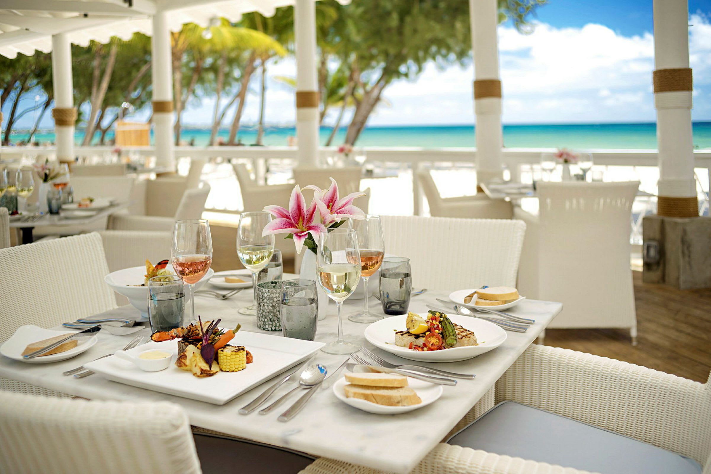 En dukad restaurangbord nära stranden med tallrikar, glas och blommor. (AI-genererad text)
