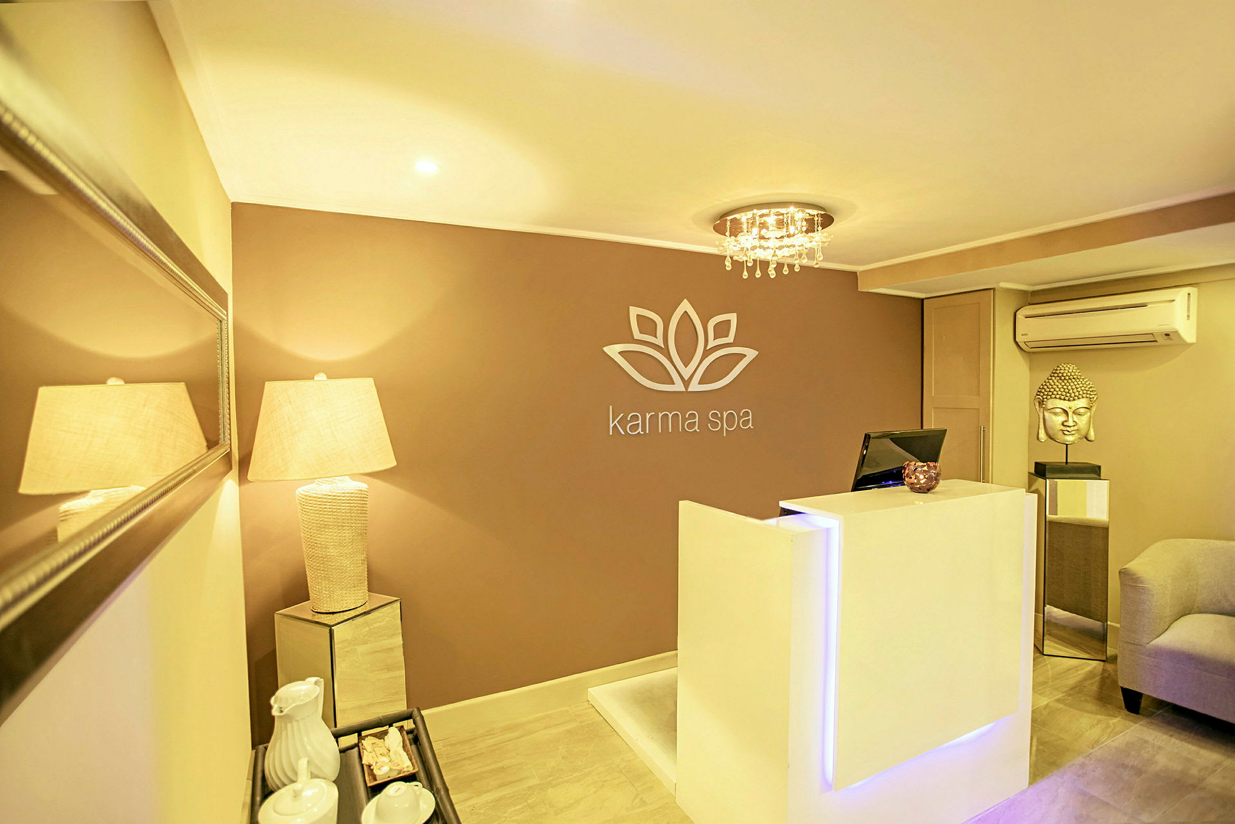 En reception i en spa-anläggning med en modern och elegant design. En vit receptionsdisk står framför en vägg med logotyp och en lampa lyser upp rummet. (AI-genererad text)