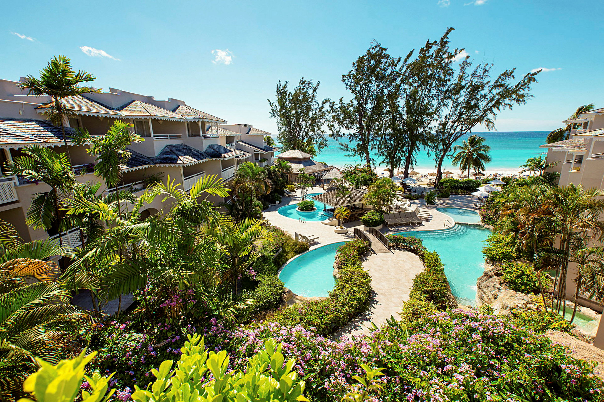Bild som visar hotellbyggnader omgivet av grönska nära en pool och stranden. (AI-genererad text)