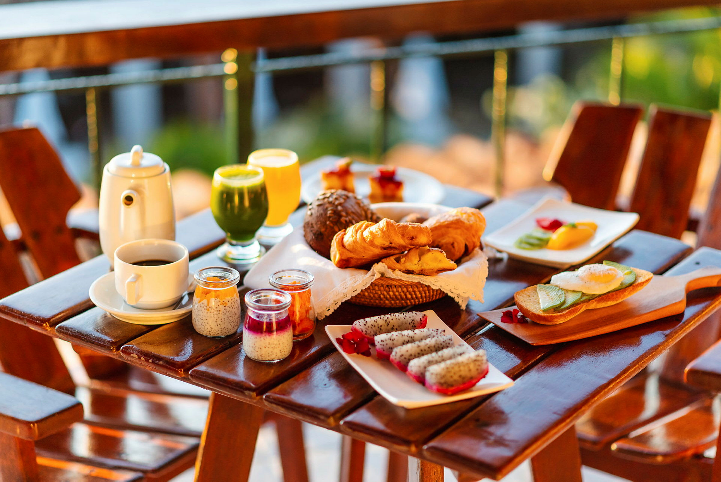 En frukost med en mängd olika maträtter som serveras på ett bord utomhus, inklusive bröd, croissanter, färsk frukt, juice och kaffe. (AI-genererad text)