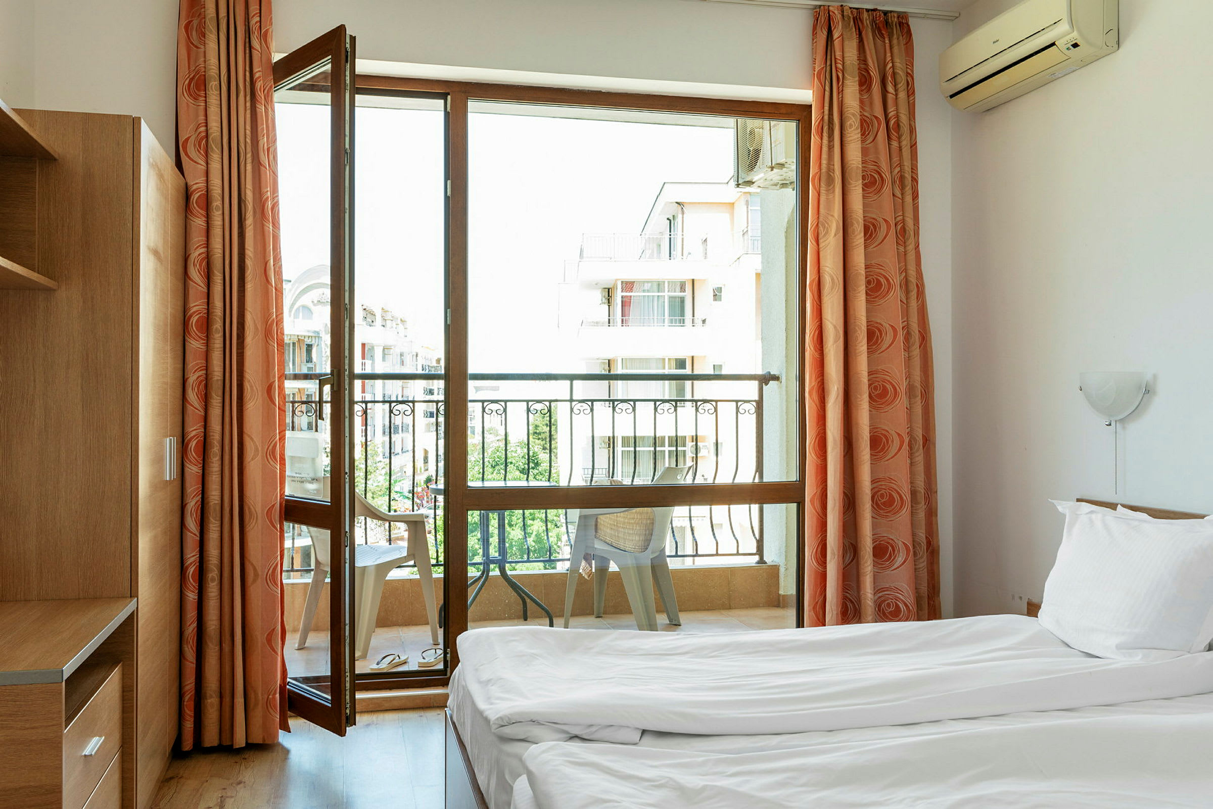 Ett hotellrum med två enkelsängar och ett fönster som leder till en balkong, där stolar står. (AI-genererad text)