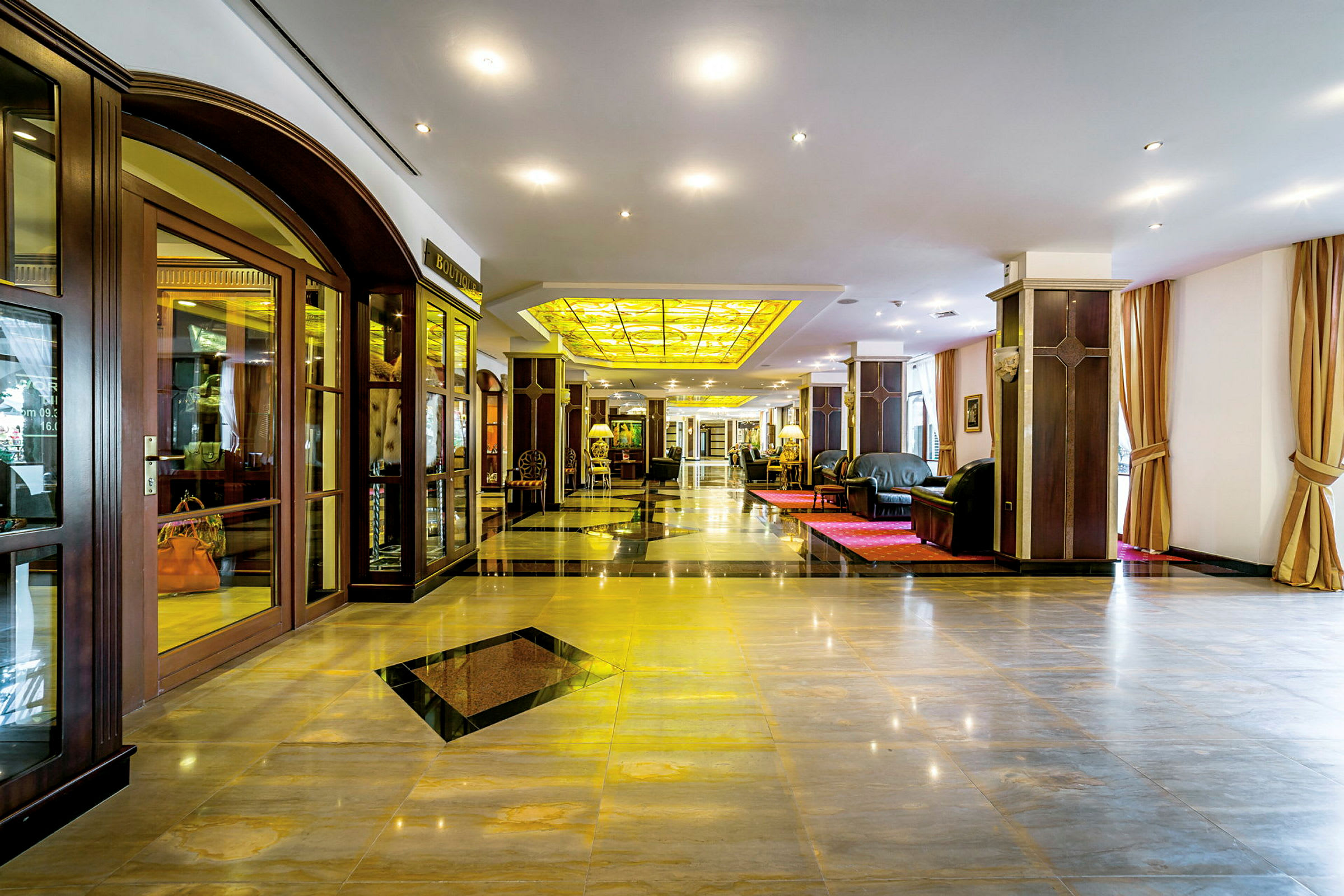 Ett elegant hotellobby med glänsande golv, bekväma soffor och ett gult glastak. (AI-genererad text)