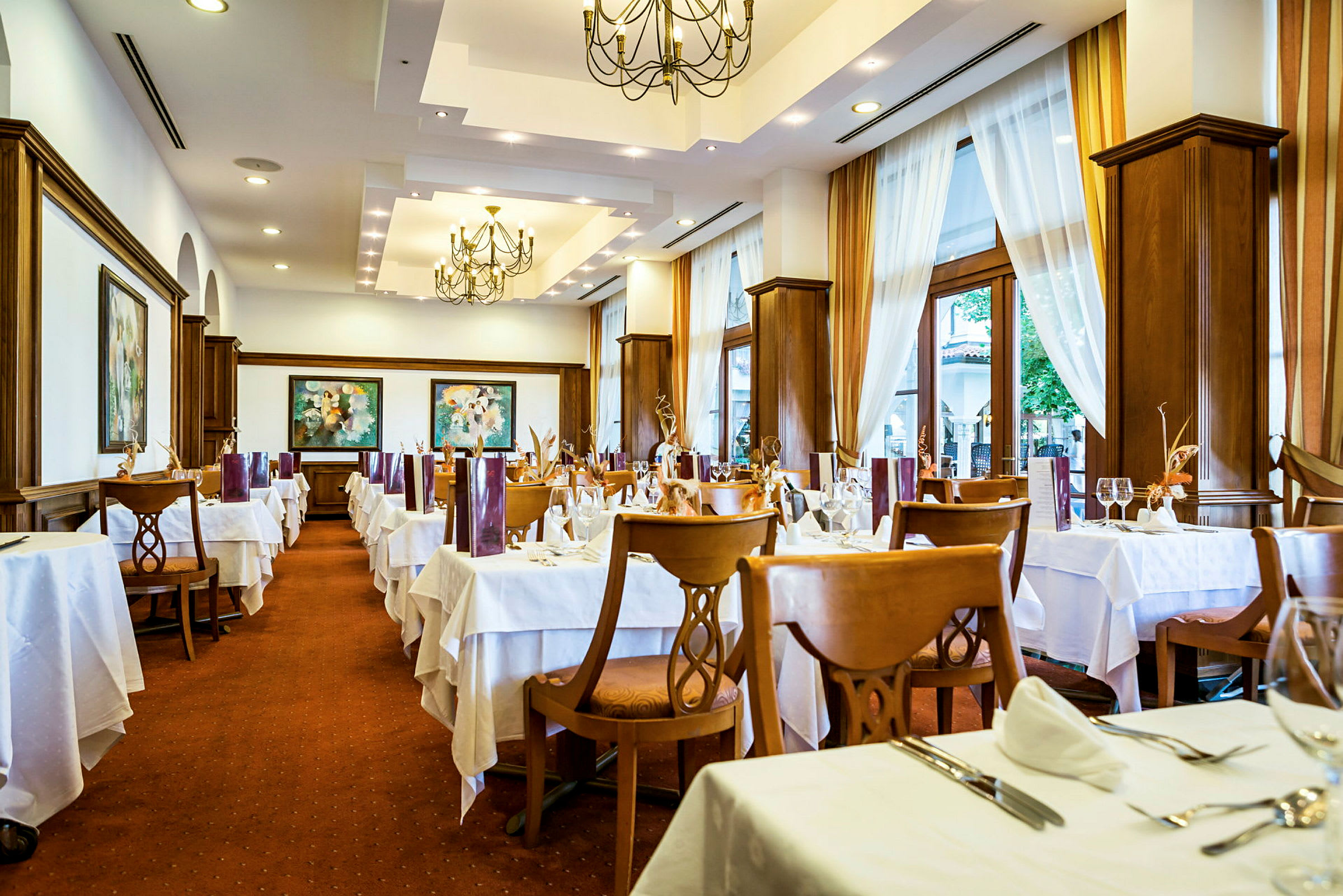 Interiör av en restaurang med dukade bord och stolar, ljusa gardiner och dekorativa taklampor. (AI-genererad text)