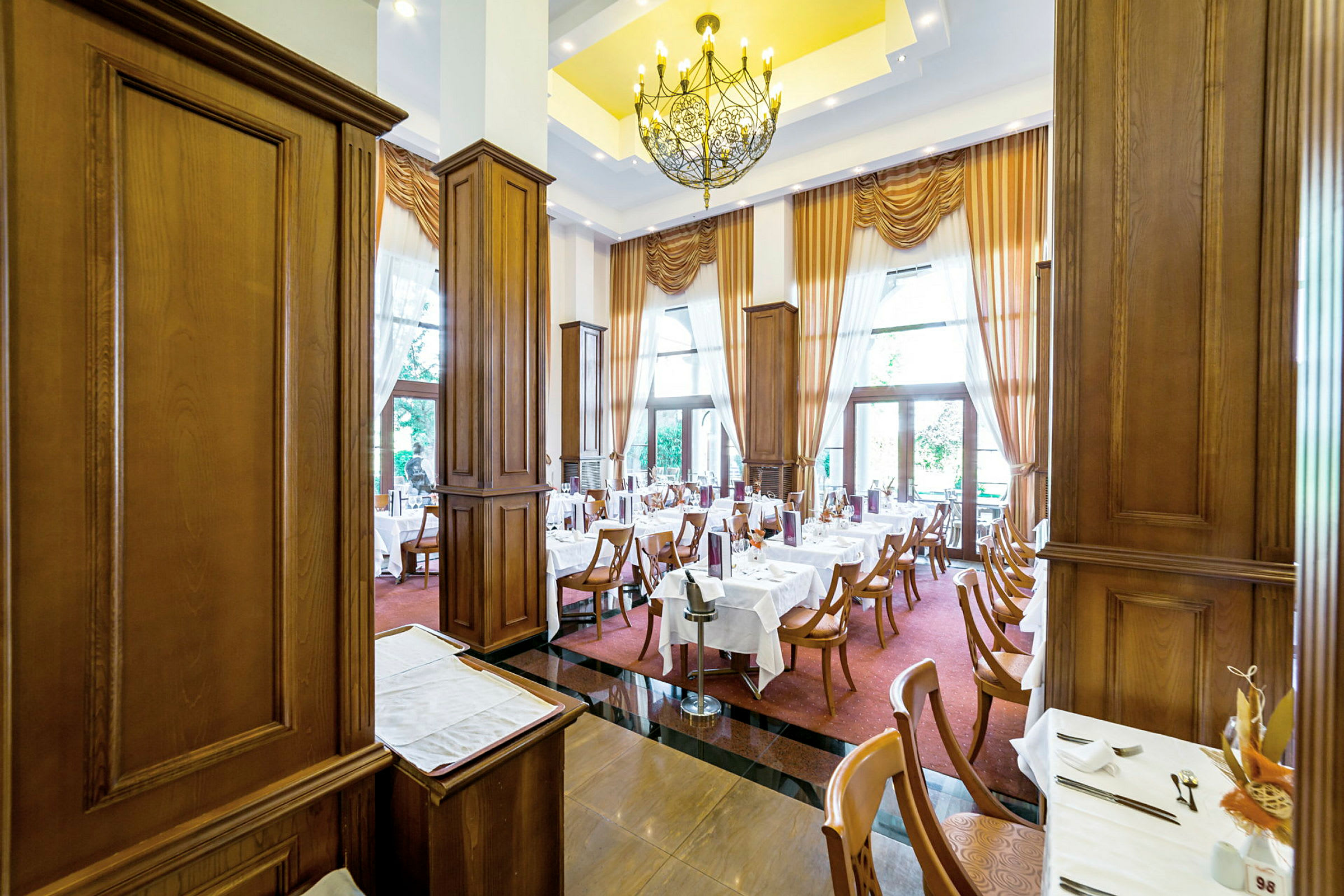 En elegant restaurang med dukade bord, träpaneler och stora fönster med gardiner. (AI-genererad text)