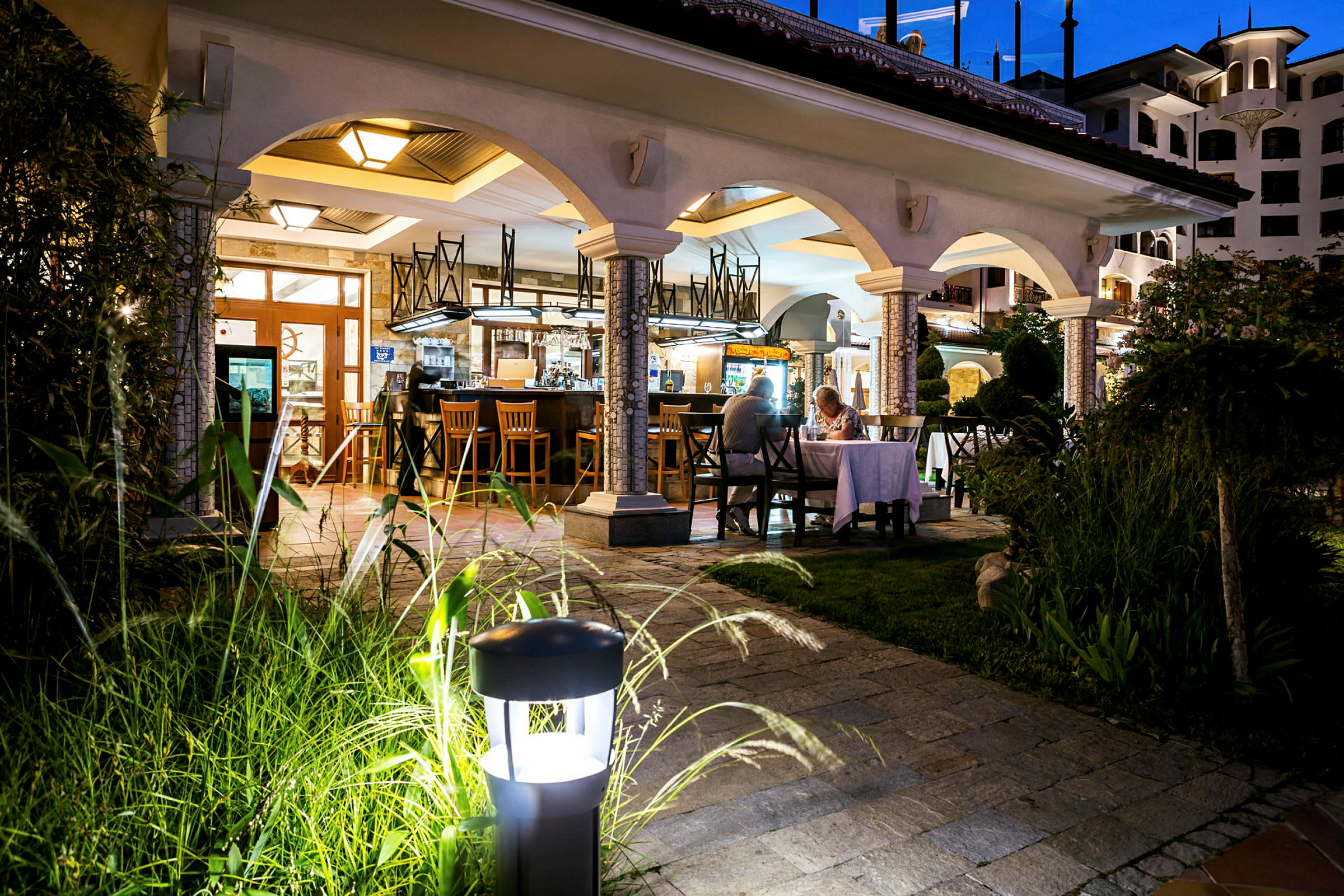 Bild av en restaurang med bågformad arkitektur, utomhusbelysning och en elegant atmosfär på kvällen. (AI-genererad text)
