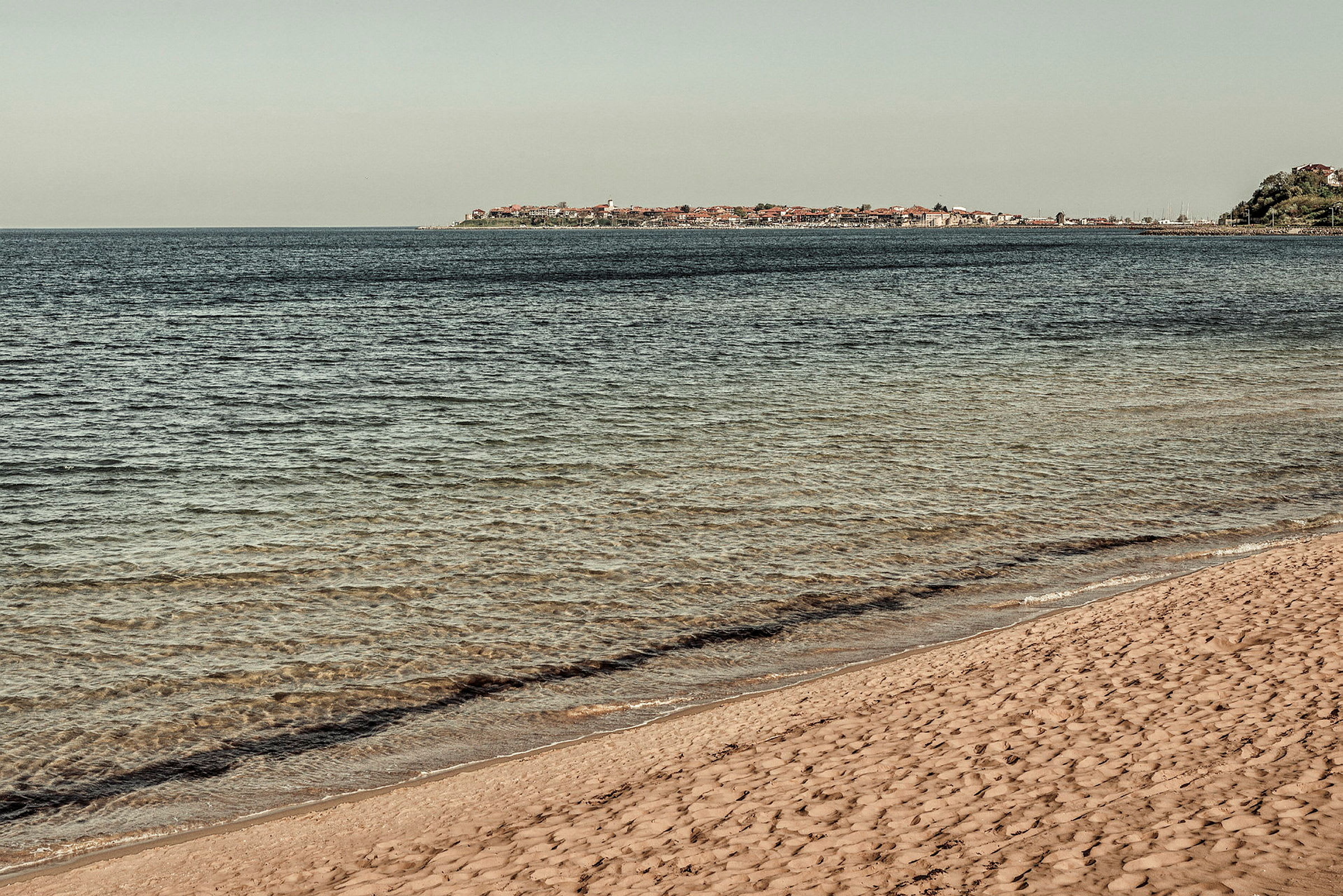 Bild av en sandstrand vid havet med en stad i bakgrunden. (AI-genererad text)