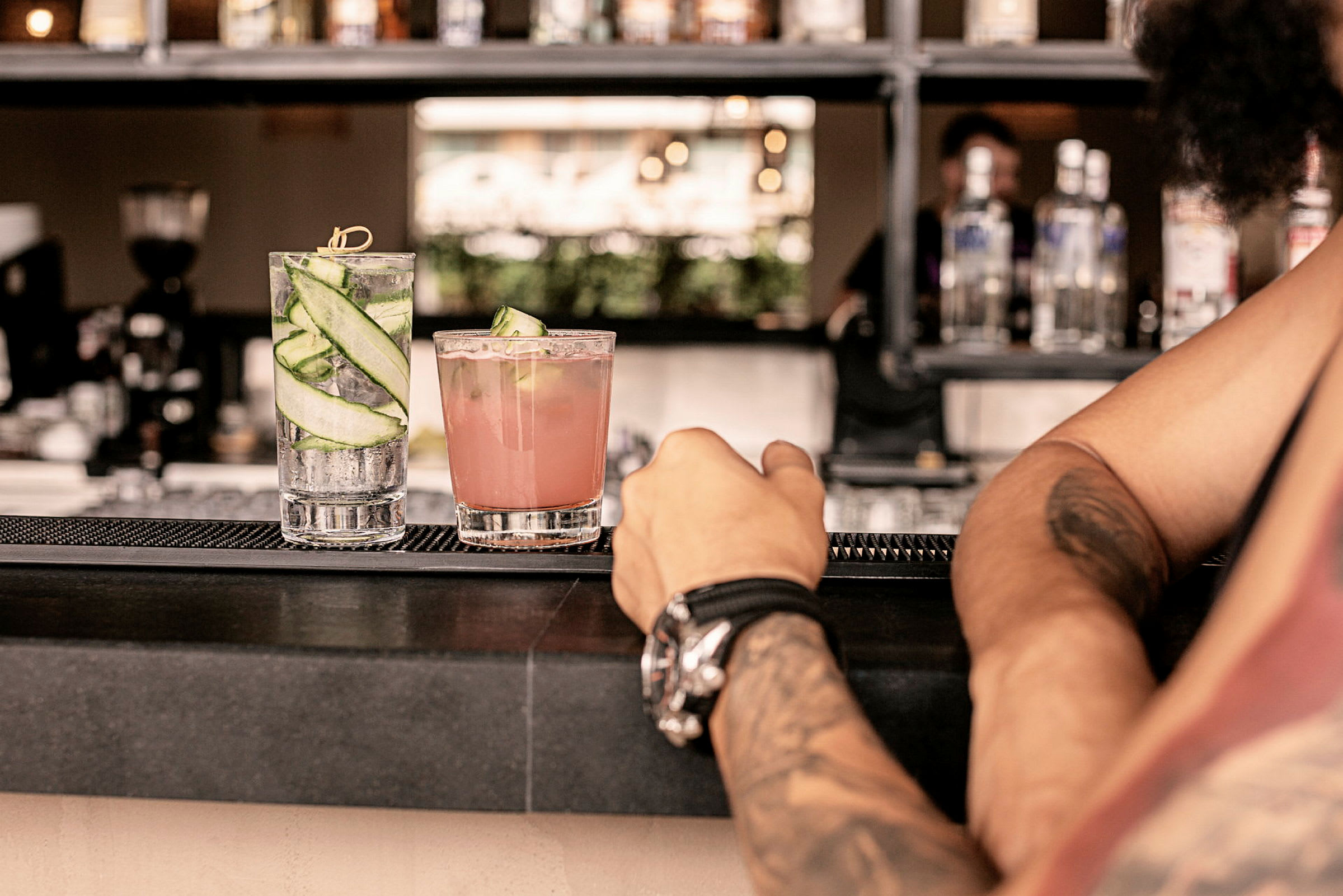Två cocktails på en bardisk, med en persons arm i förgrunden. (AI-genererad text)