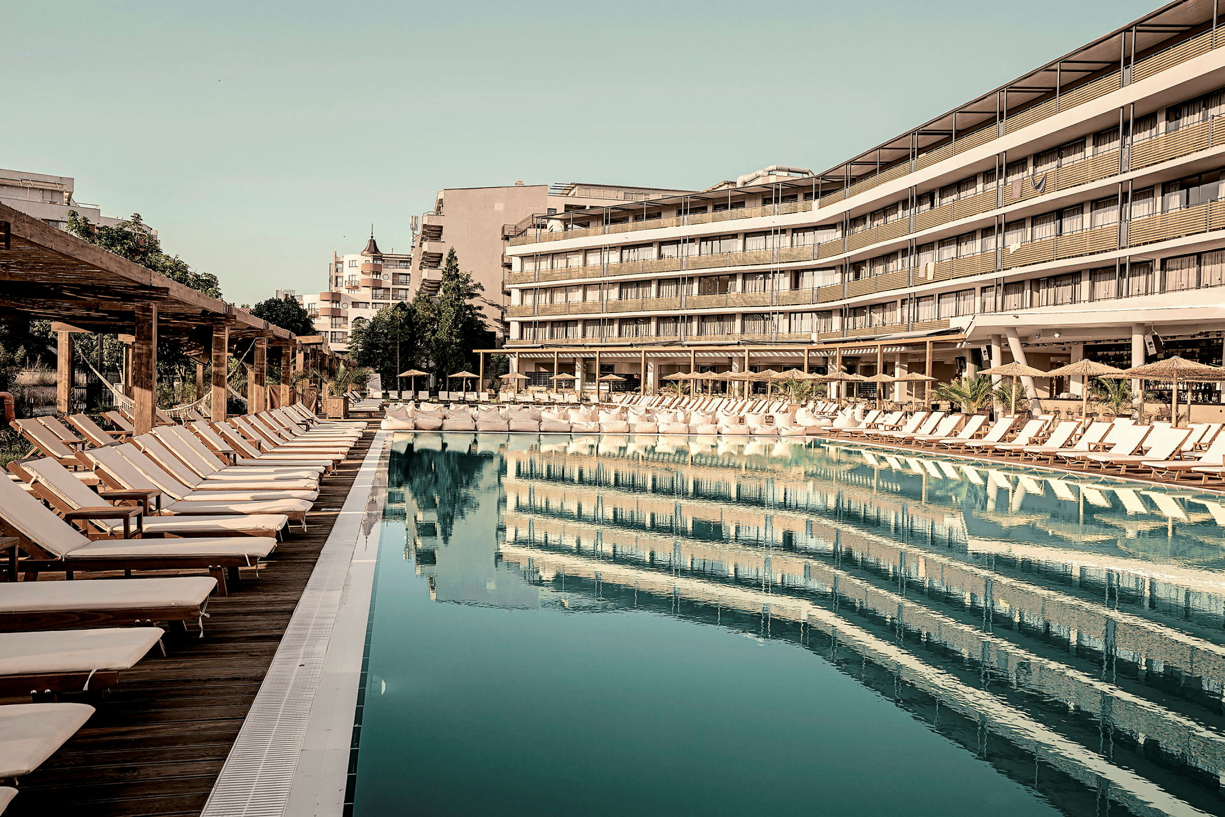 Bild av en pool med solstolar och omgivande byggnader. (AI-genererad text)