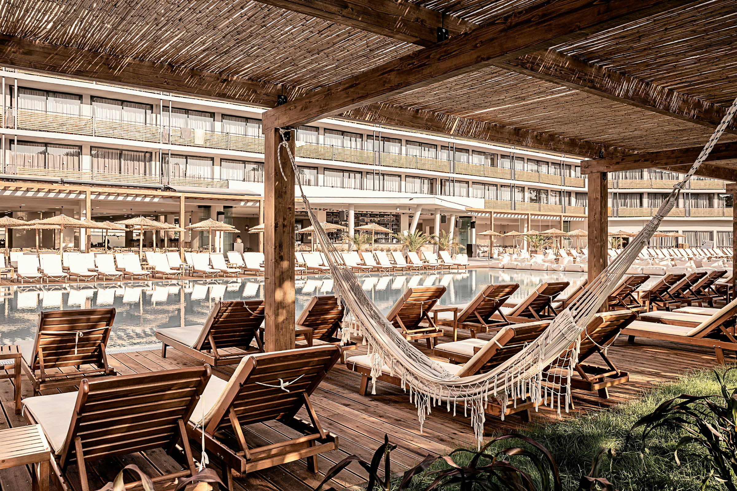 Stolar och en hängmatta vid en pool, med hotellbyggnaden i bakgrunden. (AI-genererad text)