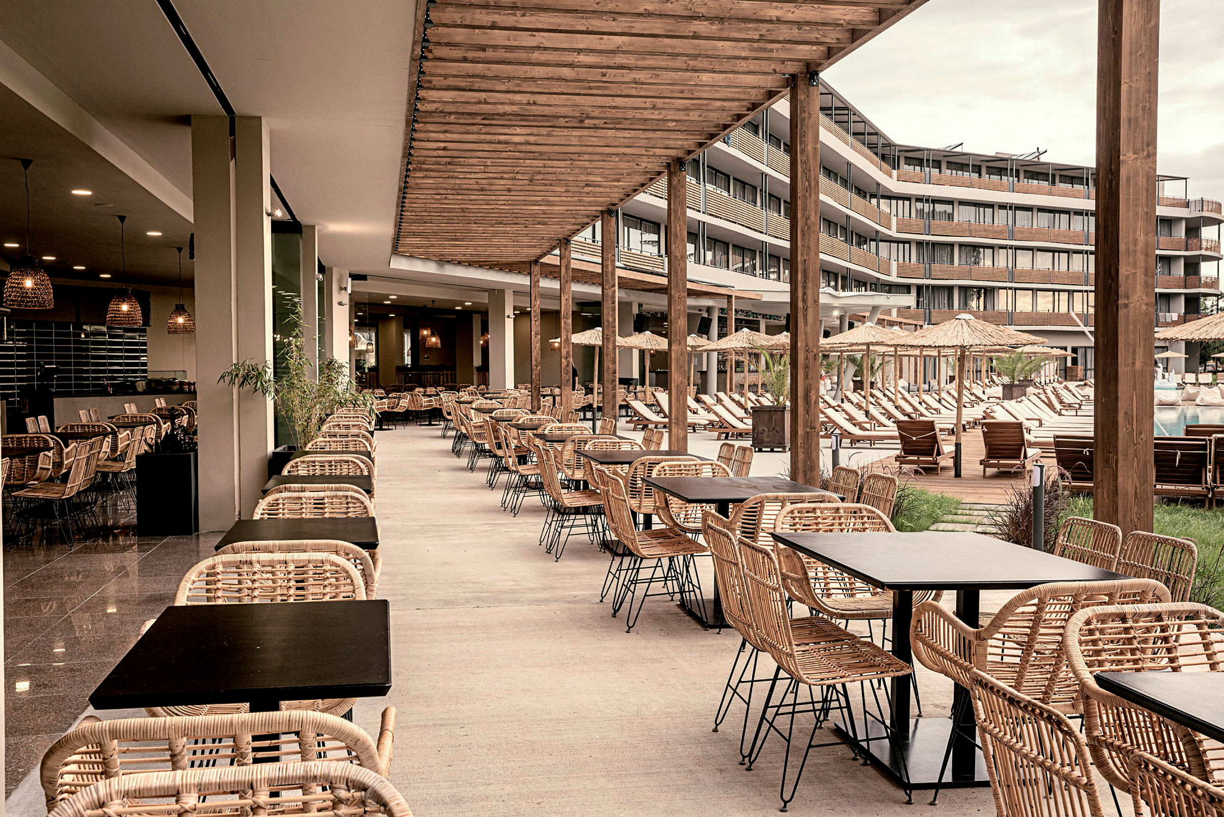 En utomhusrestaurang med rottingmöbler och utsikt över en pool och solstolar. (AI-genererad text)