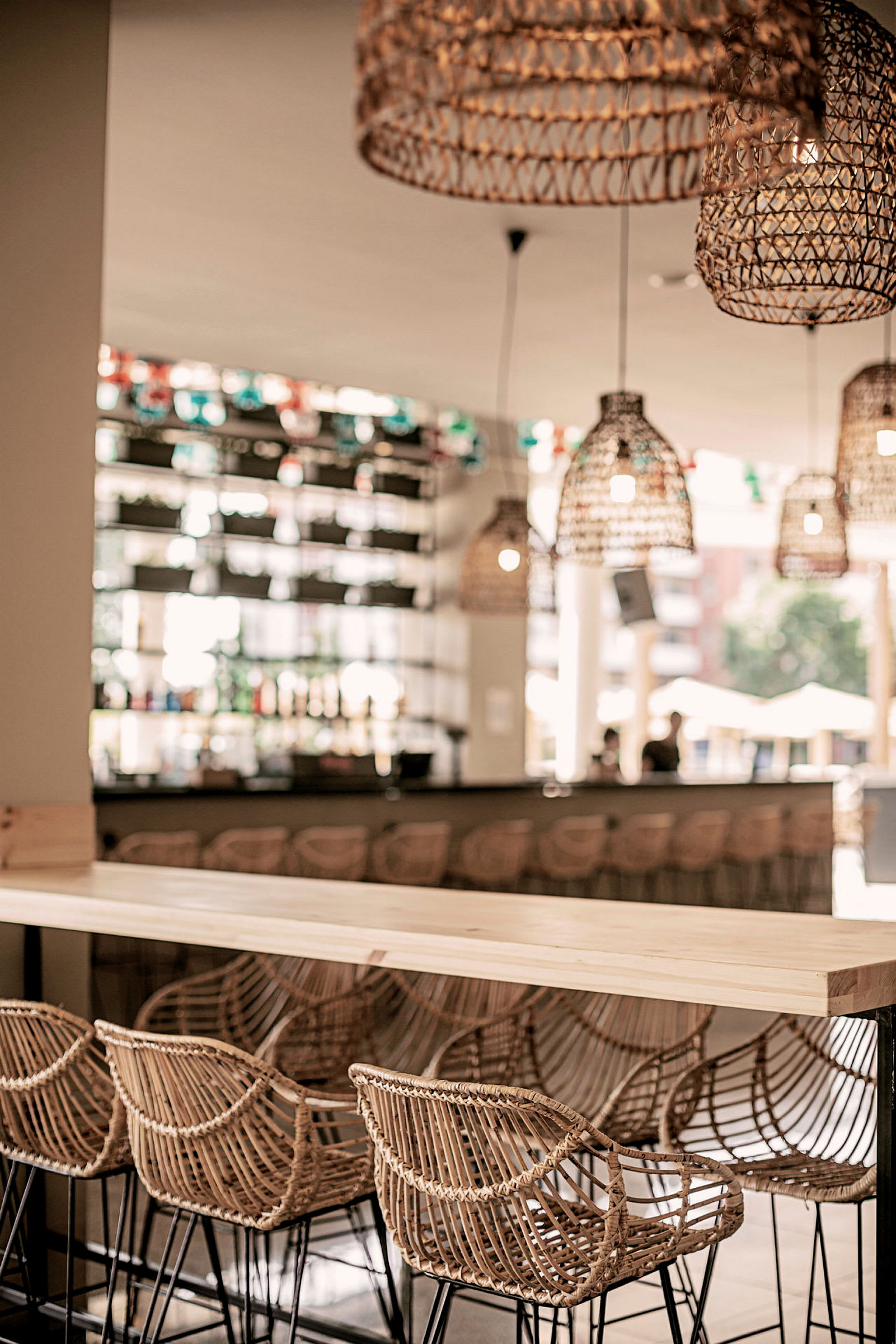 En bar med flätade stolryggar och bord av trä samt korglampor hängande från taket. (AI-genererad text)