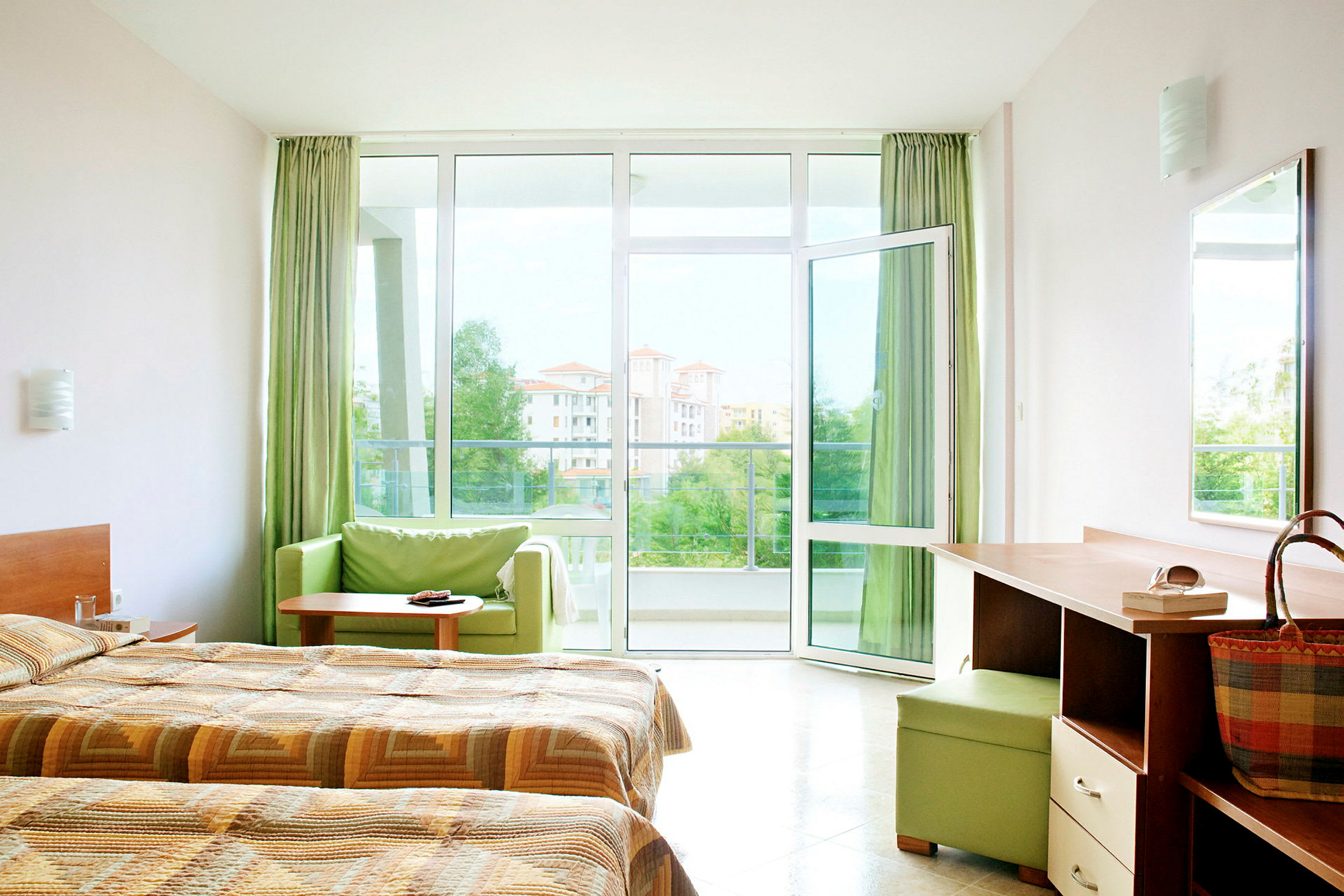 Hotellrum med dubbelsängar, skrivbord samt öppet fönster mot en balkong med utsikt. (AI-genererad text)