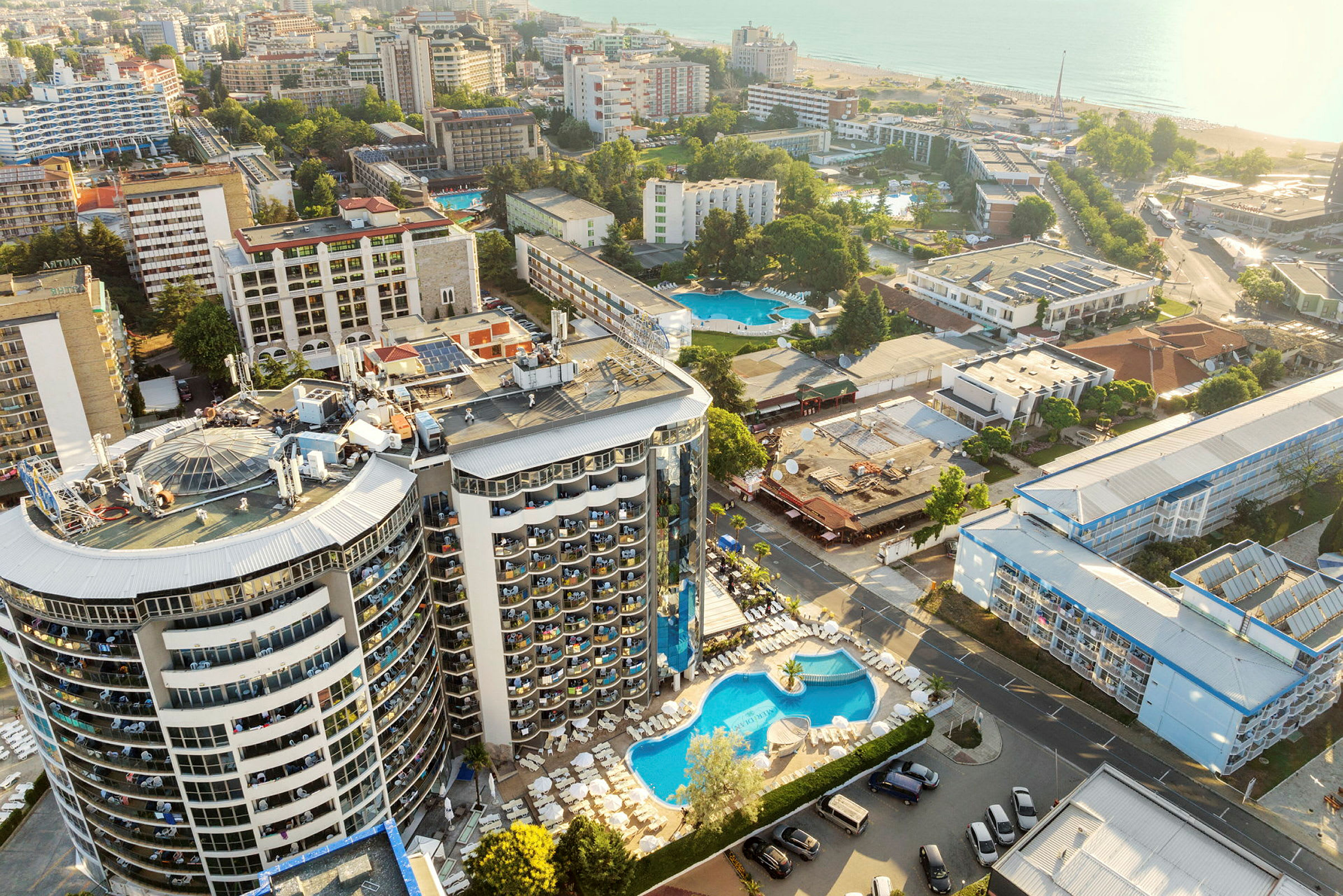 Flygfoto över hotellområde med pool och omgivande byggnader nära havet. (AI-genererad text)
