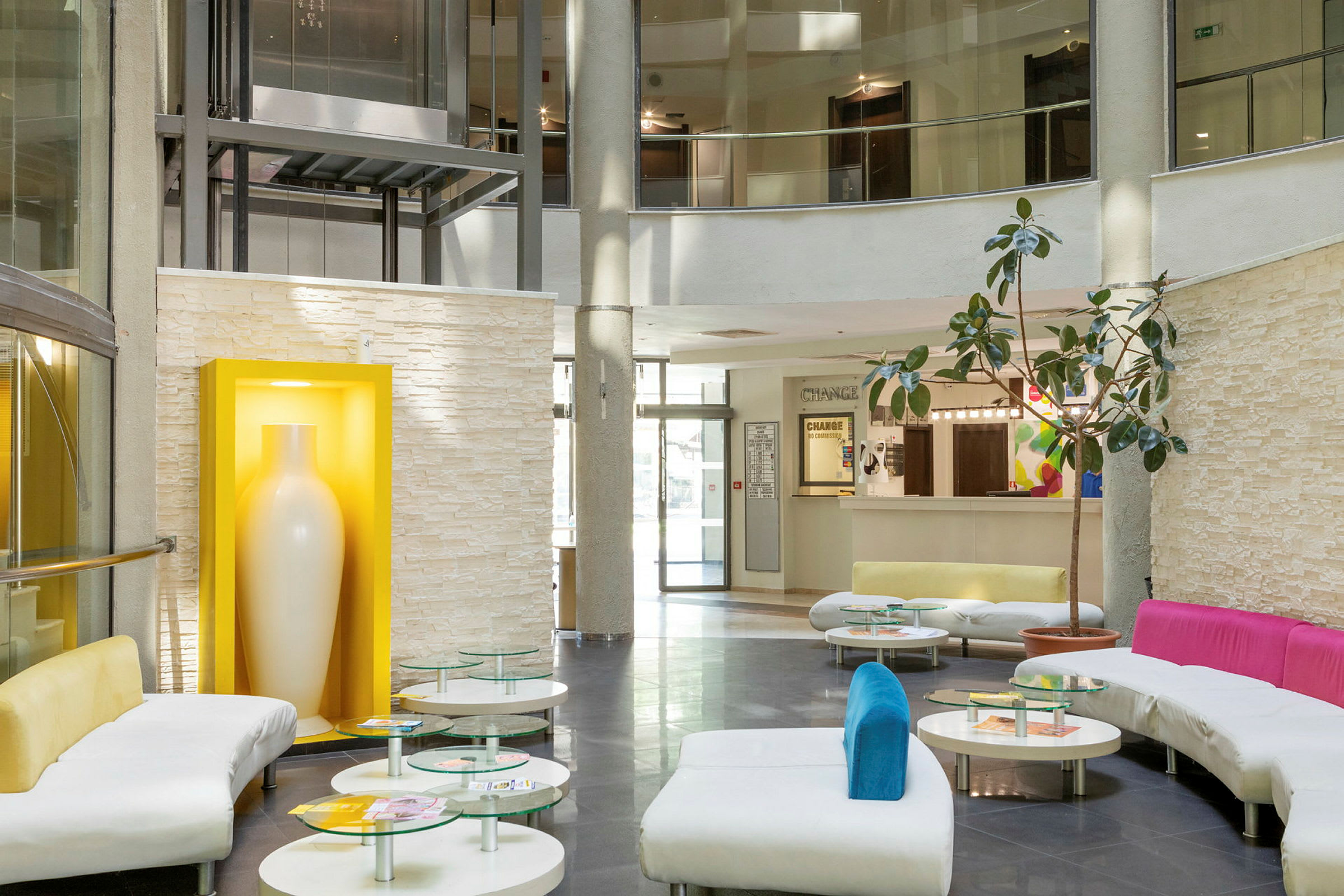 En modern hotellobby med soffor, glasbord och en stor vit vas i en gul inramning. (AI-genererad text)
