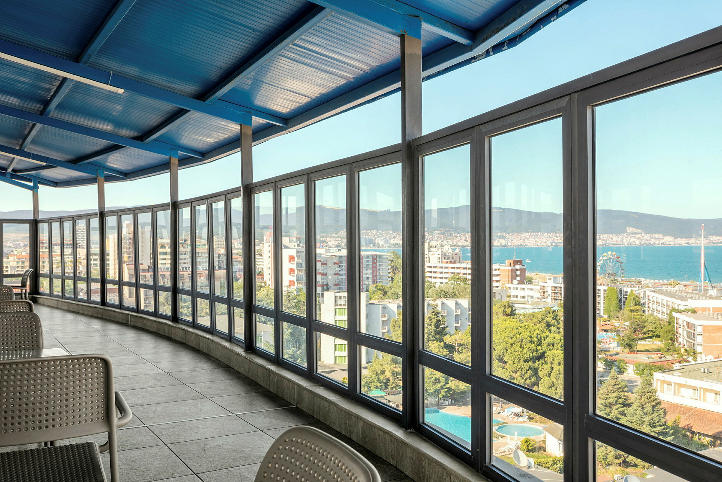 Interiör med en inglasad veranda som har utsikt över en stad och havet. (AI-genererad text)