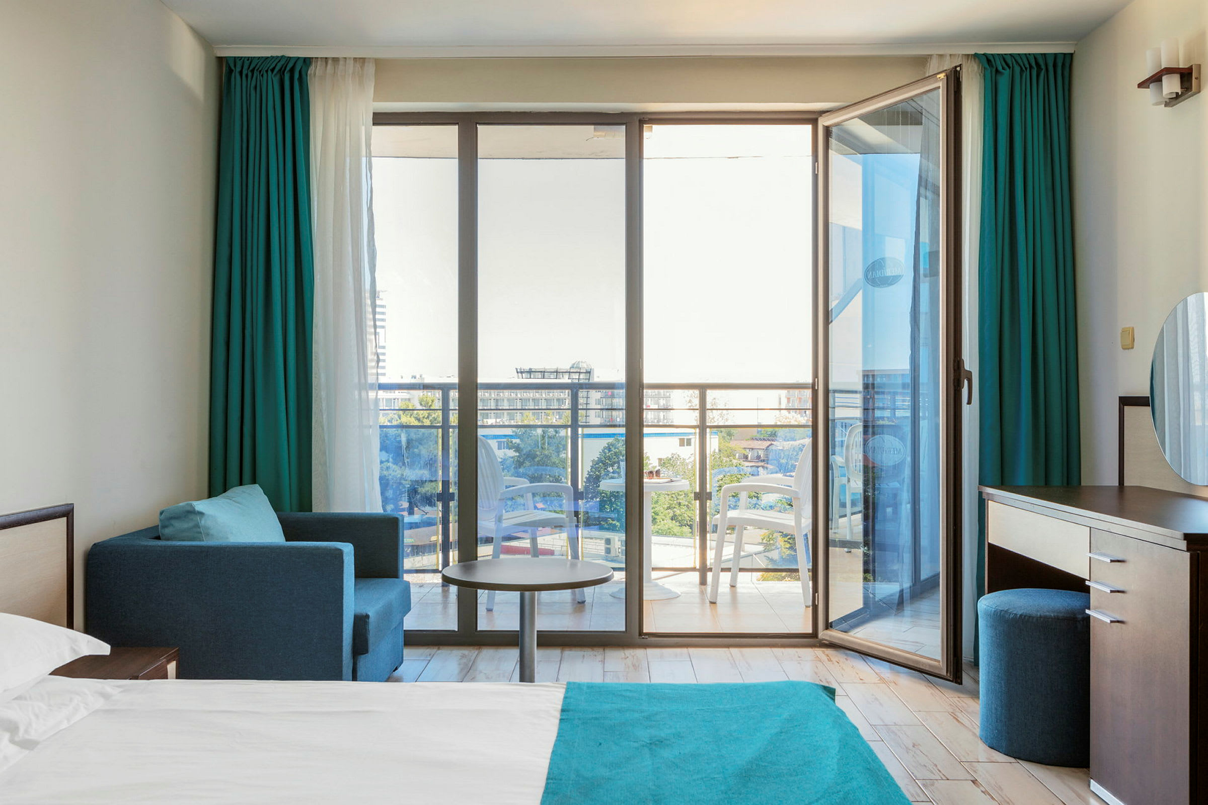 Modernt hotellrum med en säng, sittgrupp och glasdörrar mot en balkong. (AI-genererad text)