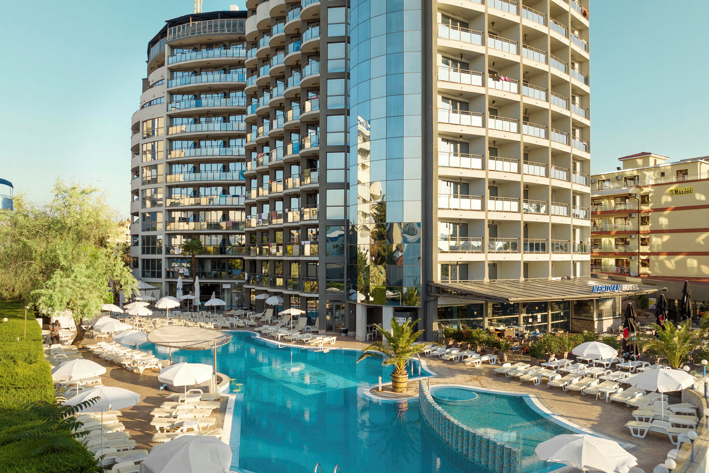 Ett hotellkomplex med en pool omgiven av solstolar och paraplyer. (AI-genererad text)