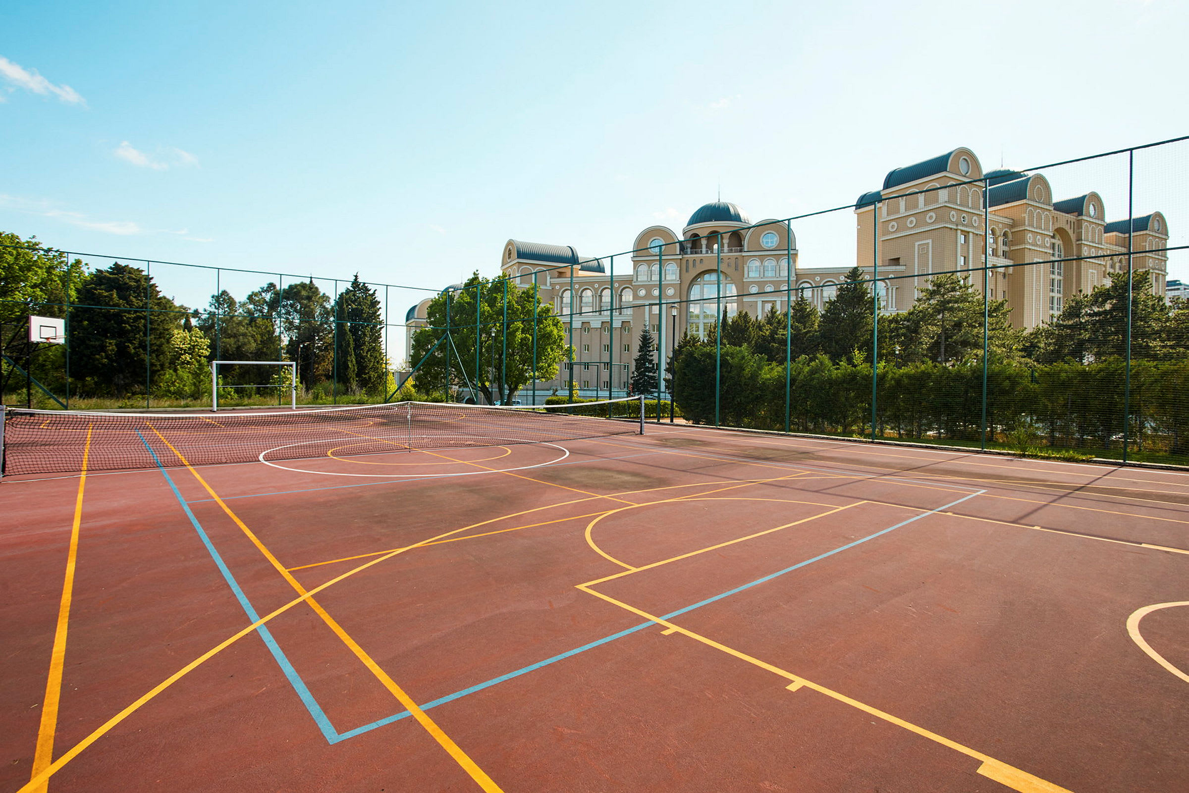 En idrottsplan med basketkorg och målburar. I bakgrunden syns byggnader och grönska. (AI-genererad text)