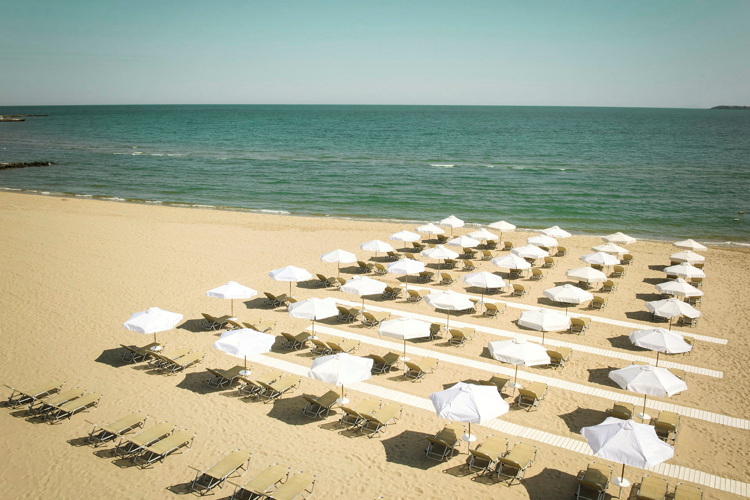 Strand med solstolar och vita parasoller vid havet. (AI-genererad text)